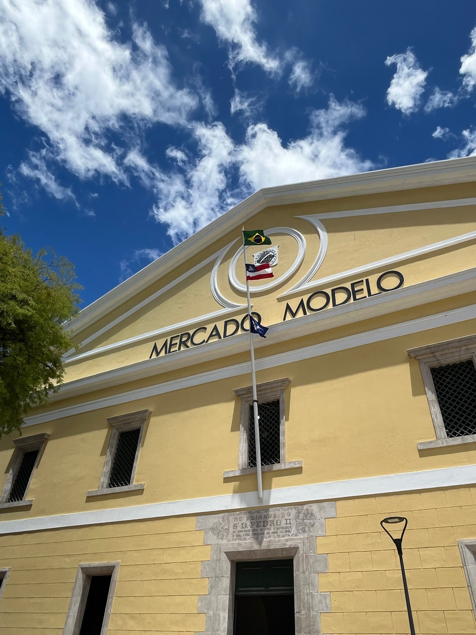 Mercado Modelo em Salvador sob céu azul com bandeiras do Brasil e da Bahia.