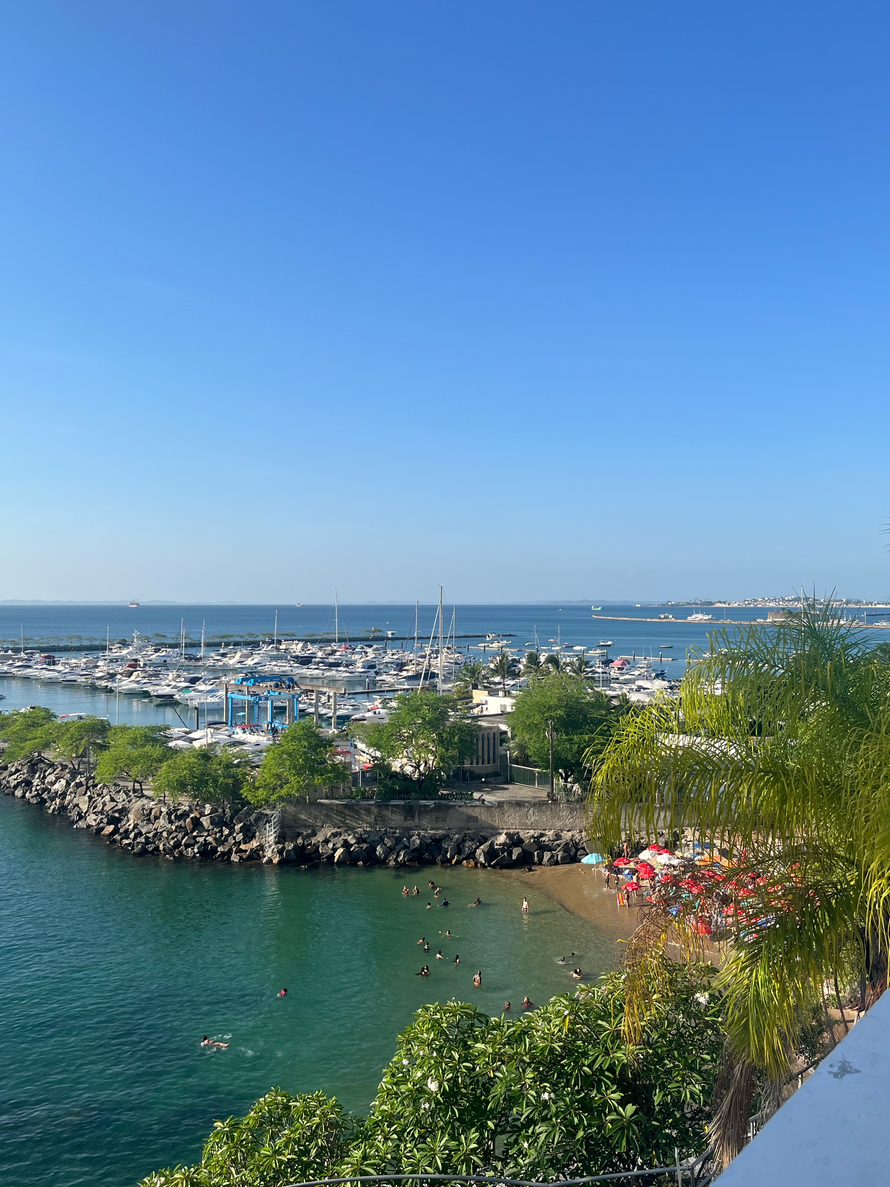 Praia em Salvador com águas cristalinas, pessoas nadando e barcos ao fundo. Ideal para relaxar e curtir o dia.