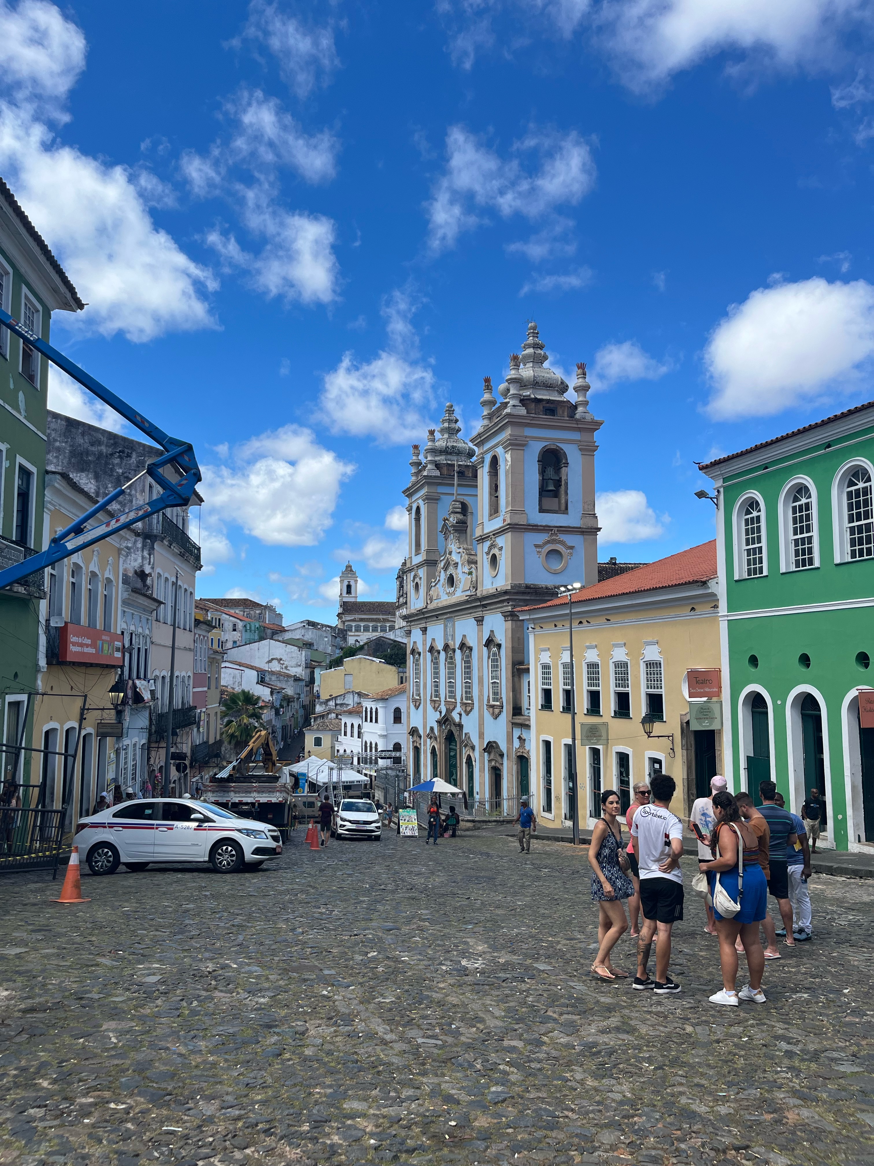 Rua de paralelepípedos no Pelourinho, Salvador, com igrejas coloniais ao fundo e turistas passeando.