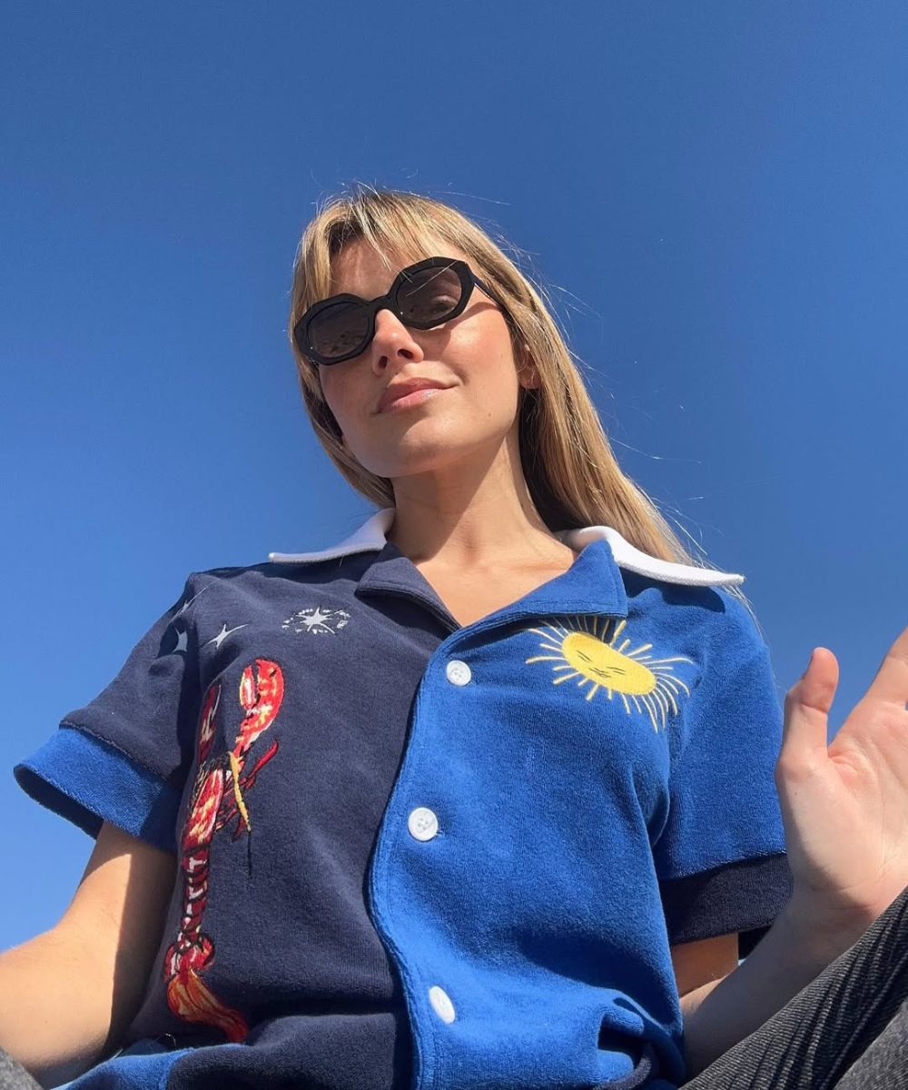 Pessoa usando camisa azul com desenho de sol e lagosta, em cenário ensolarado.