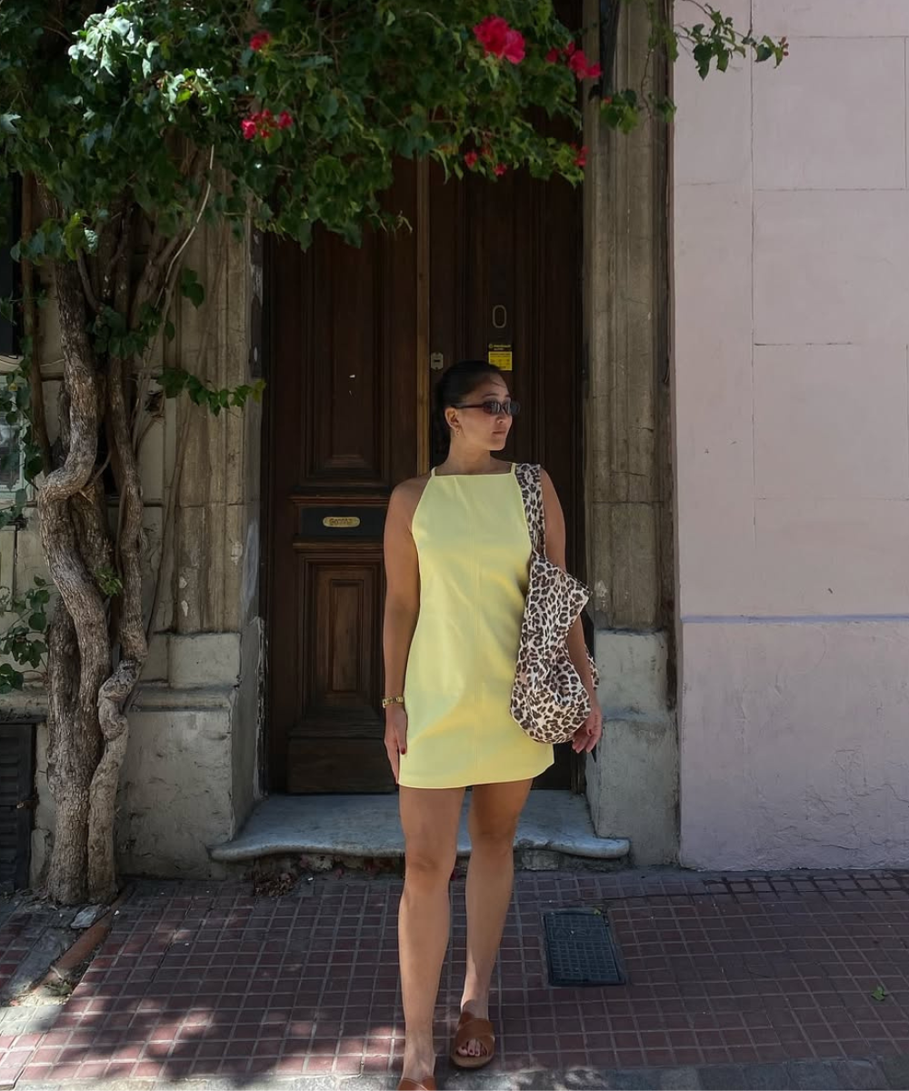 Mulher com vestido amarelo, bolsa de estampa de animal, de pé em frente a porta durante viagem no verão.