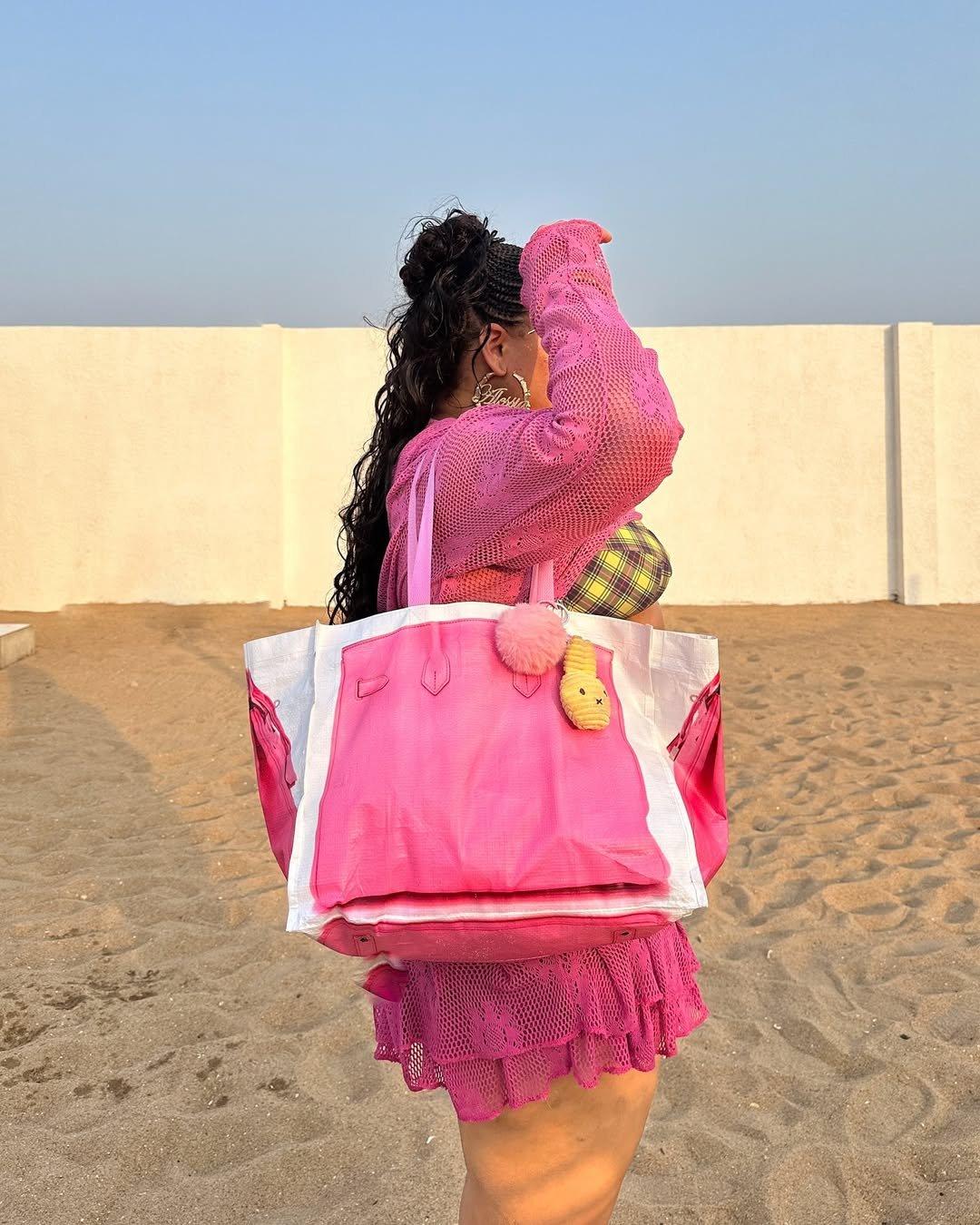 Mulher de vestido rosa segura maxi bolsa rosa na praia.