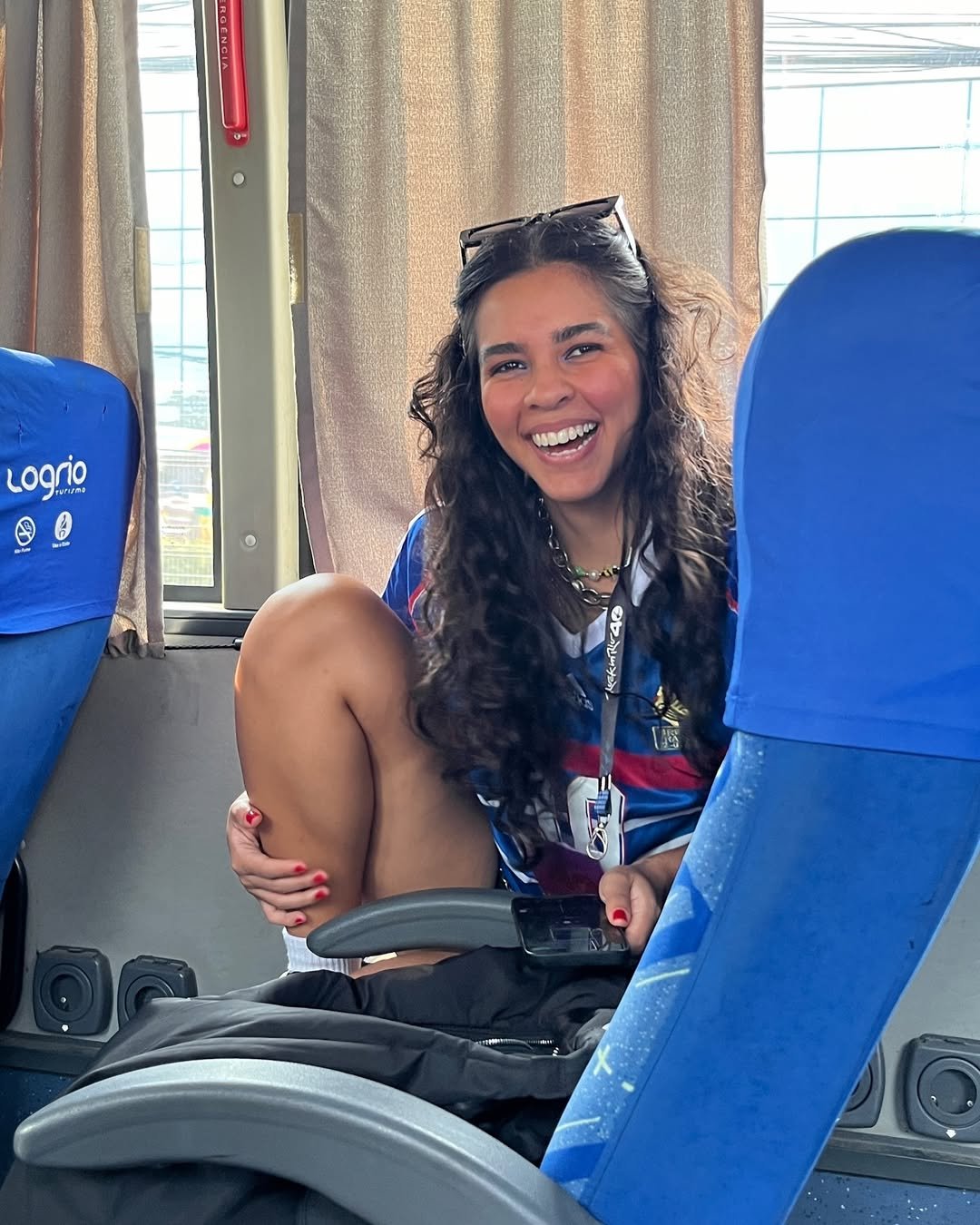 Uma pessoa sorridente em um ônibus, com uma camisa colorida e cabelos cacheados. Perfumes nacionais femininos podem complementar momentos assim vibrantes. perfumes nacionais femininos e masculinos