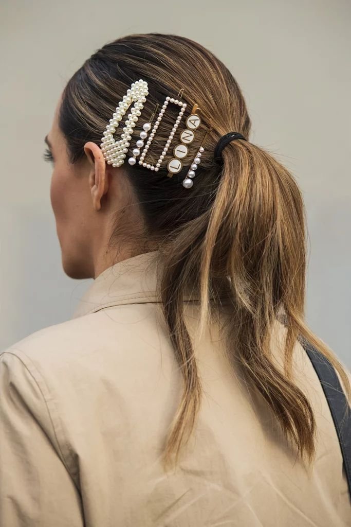 Presilha ornamentada com pérolas e letras no cabelo, tendência de acessório da moda de 2025.