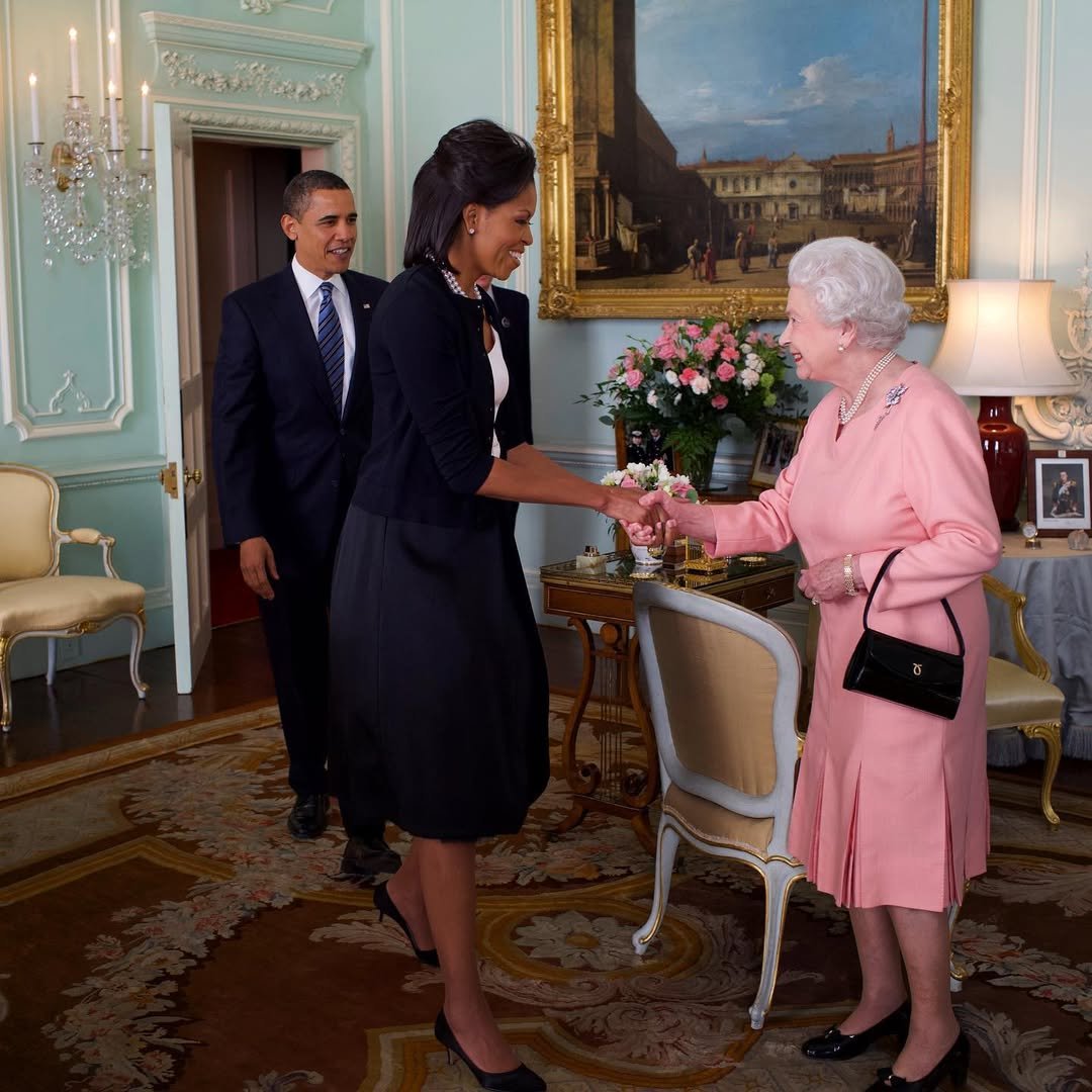 Pessoas cumprimentam-se em sala elegante. Mulher de preto, possivelmente das primeiras-damas, e idosa vestida de rosa.