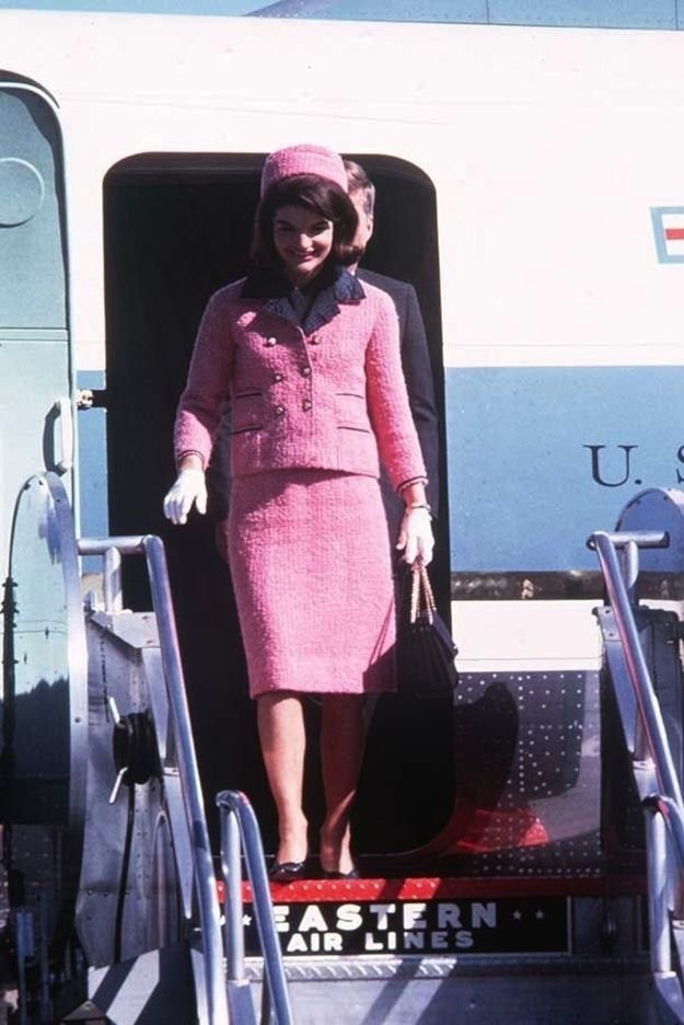 Uma mulher elegante em traje rosa desce do avião. Relação com o tema primeiras-damas.