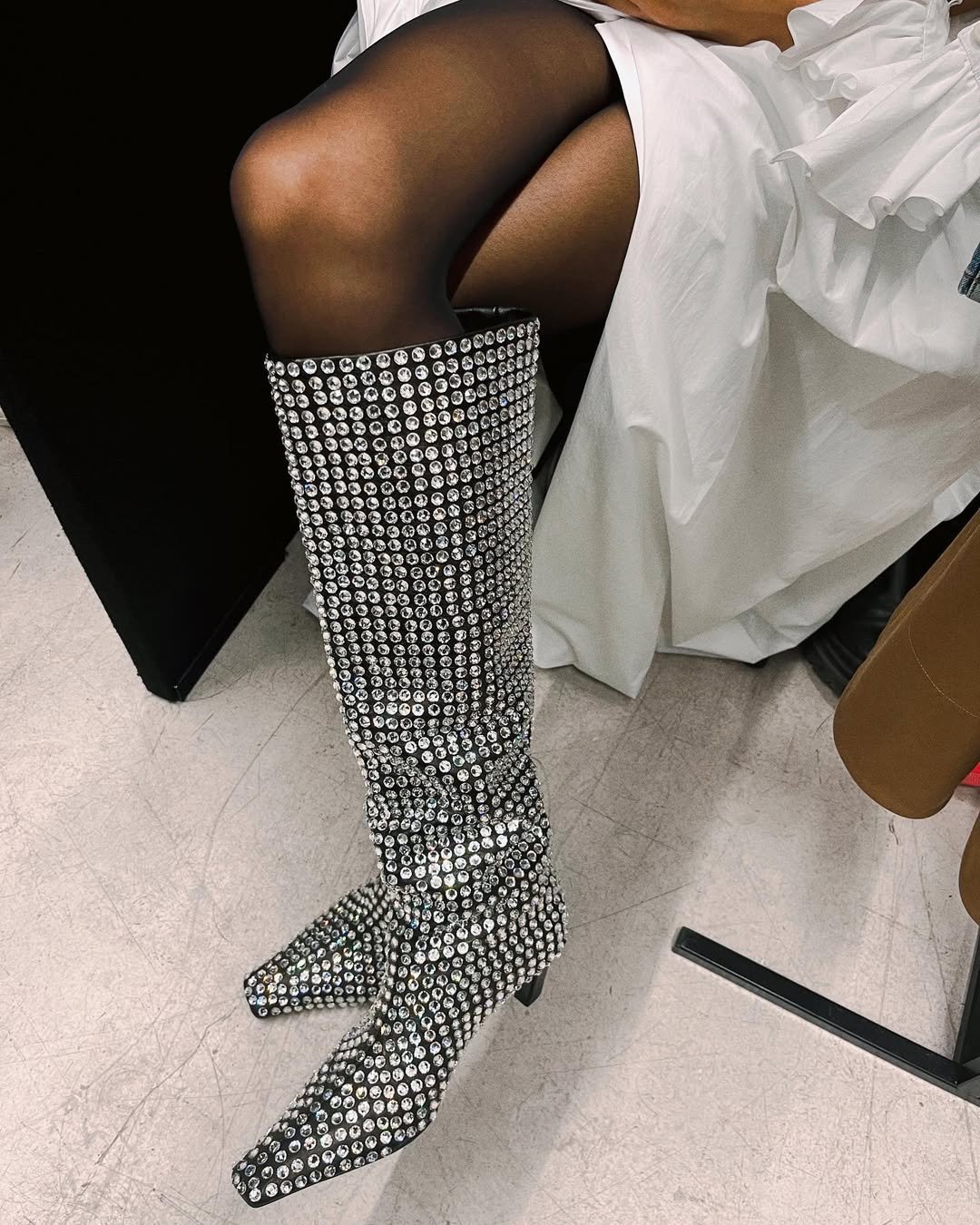 Botas prateadas cravejadas de cristais, usadas com meia-calça preta e vestido branco elegante. Resoluções de estilo.