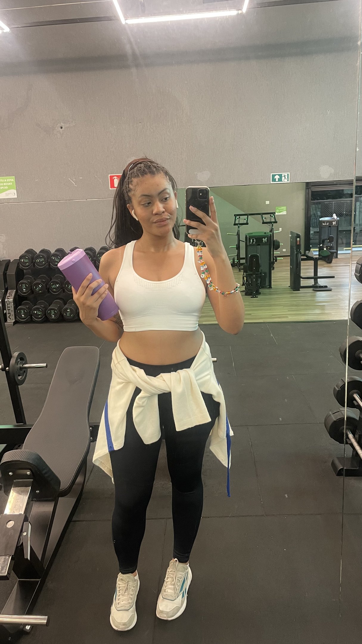 Mulher tirando selfie na academia, segurando garrafa esportiva, pronta para rotina de exercícios.