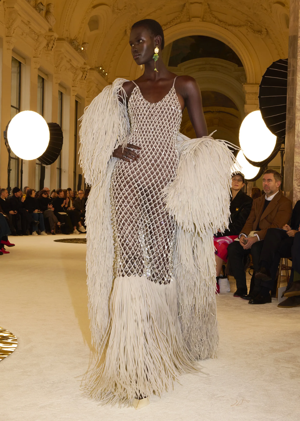 Modelo usando vestido com franjas e padrão geométrico, desfilando na Semana de Alta-Costura 2025.
