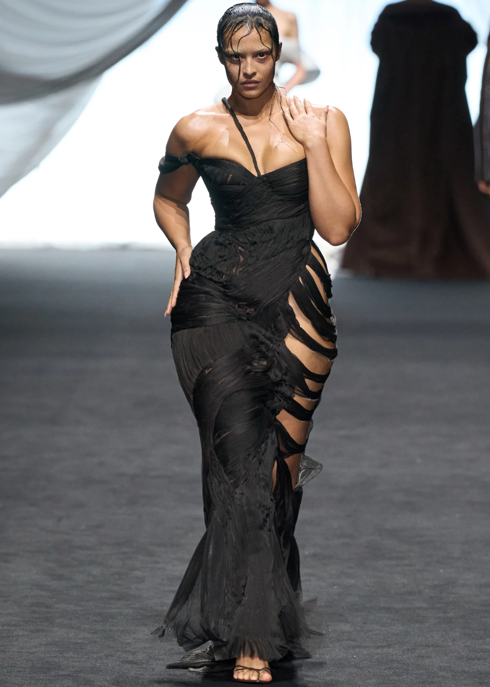 Modelo desfila em vestido preto elegante com detalhes rasgados na Semana de Alta-Costura 2025.