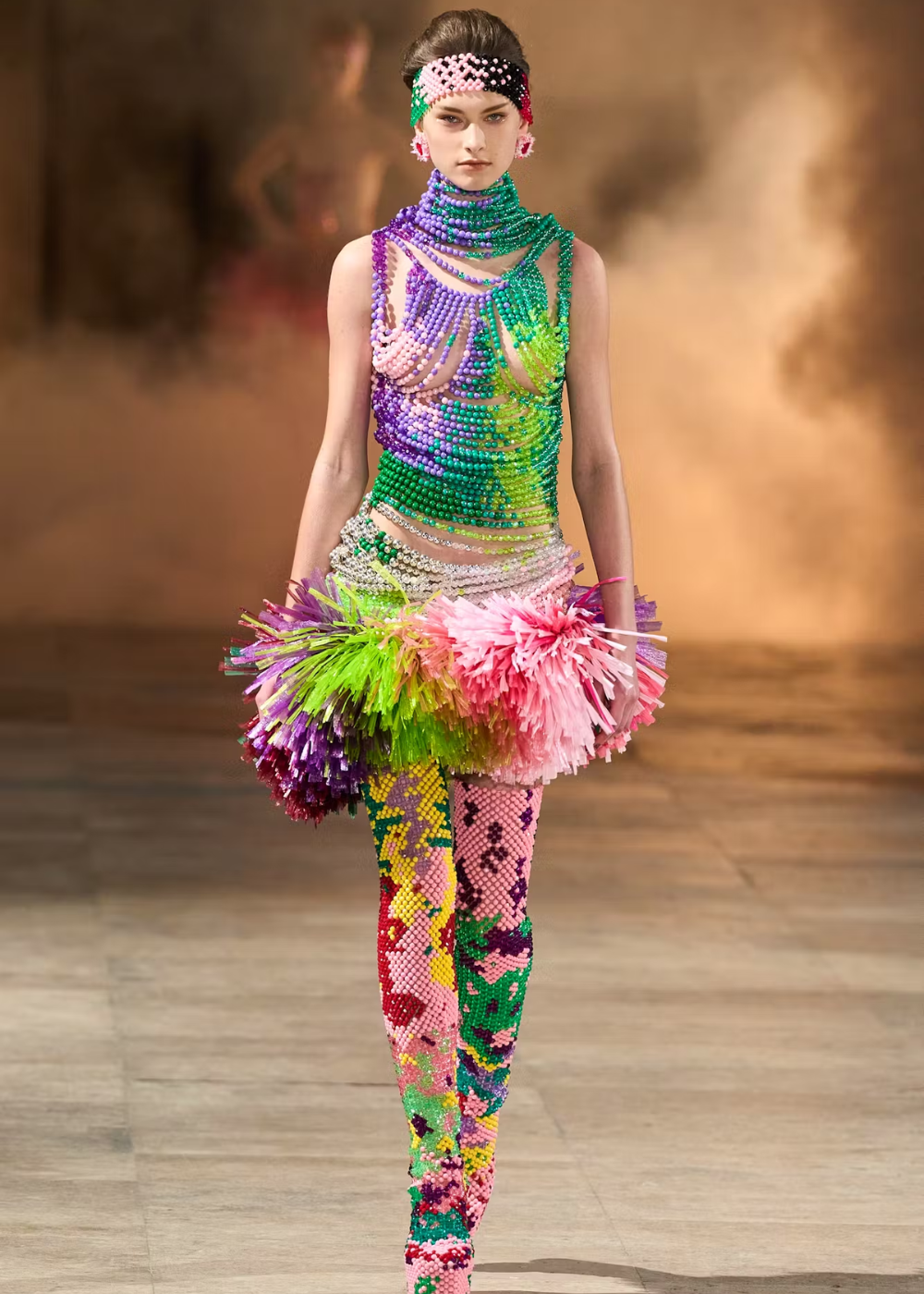Desfile de moda com modelo em traje vibrante de miçangas e pompons, remetendo à Semana de Alta-Costura 2025.