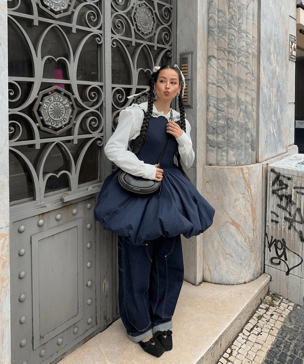 Pessoa em roupas modernas posando em frente a portão ornamentado. Elementos de moda explorando tendências polêmicas.