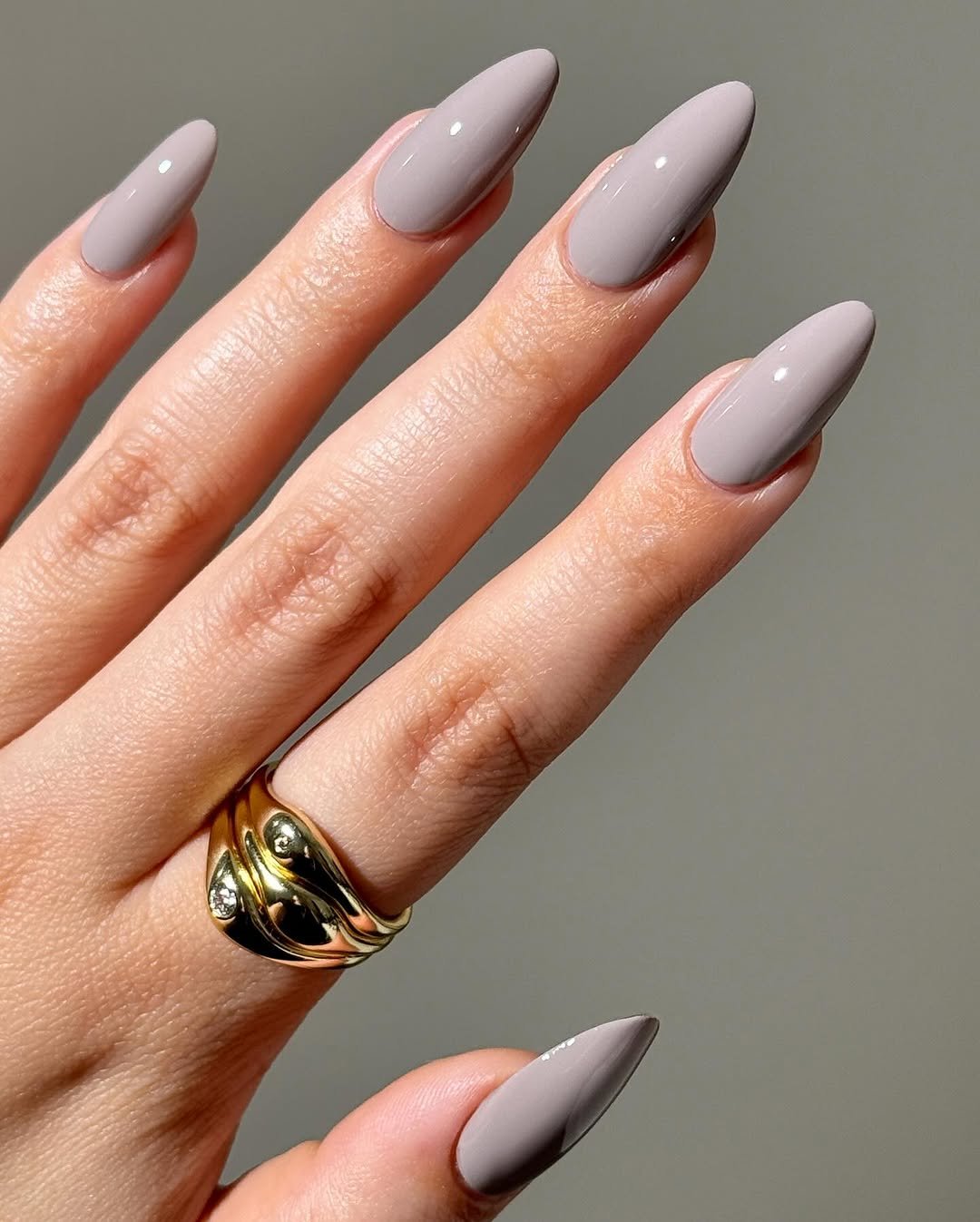 Mão com unhas básicas em tom nude e anel dourado.