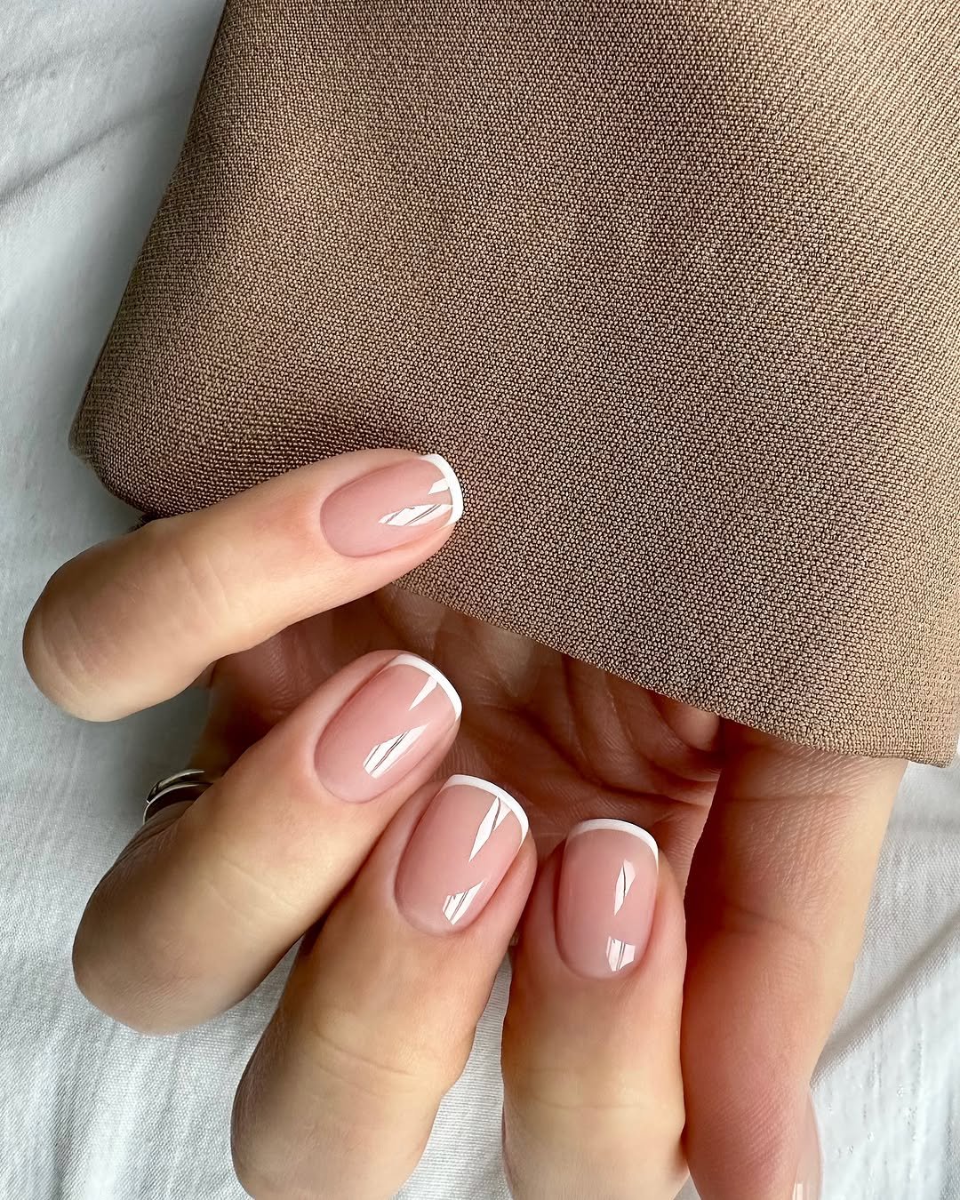 Unhas básicas com esmalte nude e detalhe branco, segurando tecido bege.