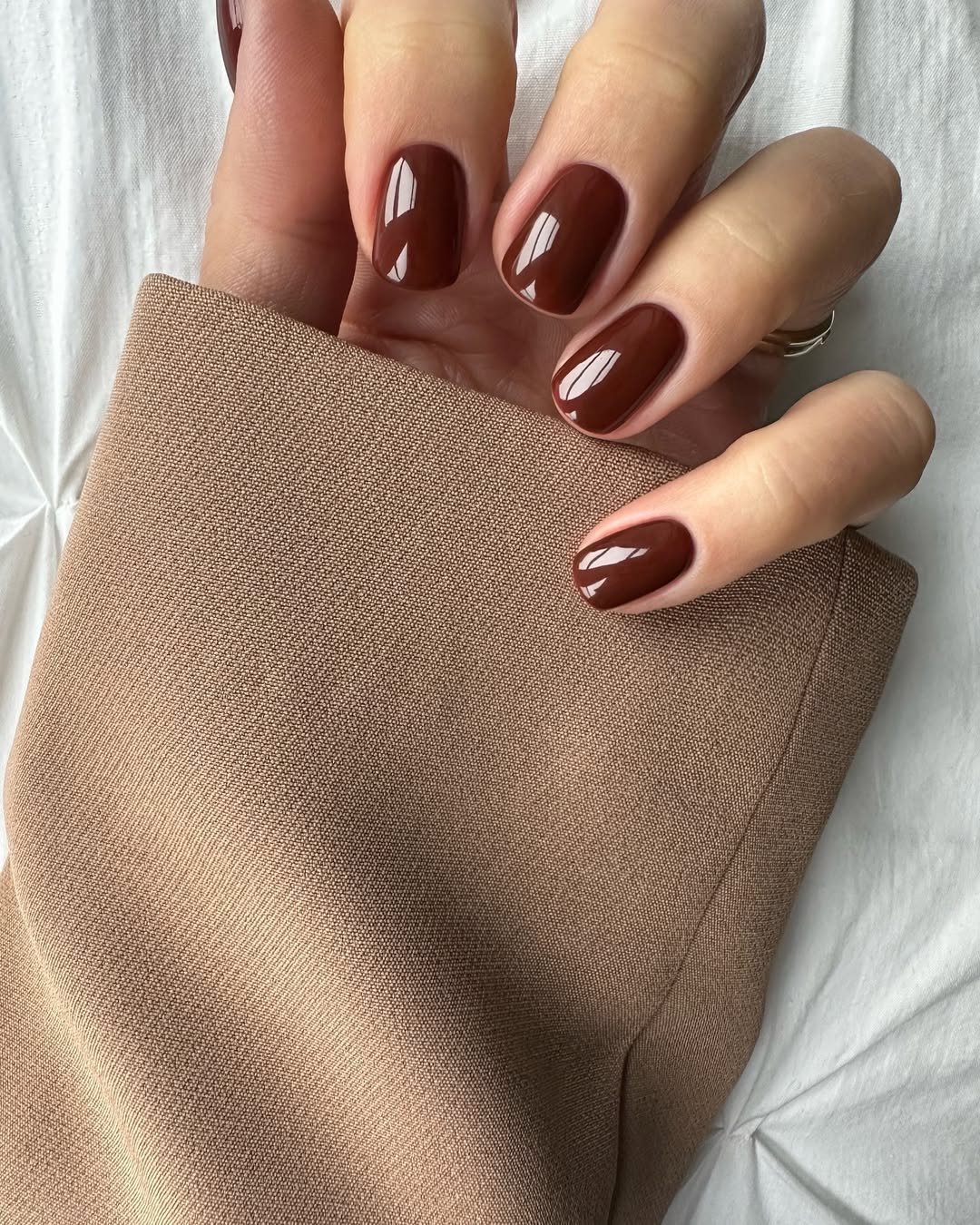 unhas básicas pintadas de marrom sobre tecido bege, destacando estilo básico e elegante.