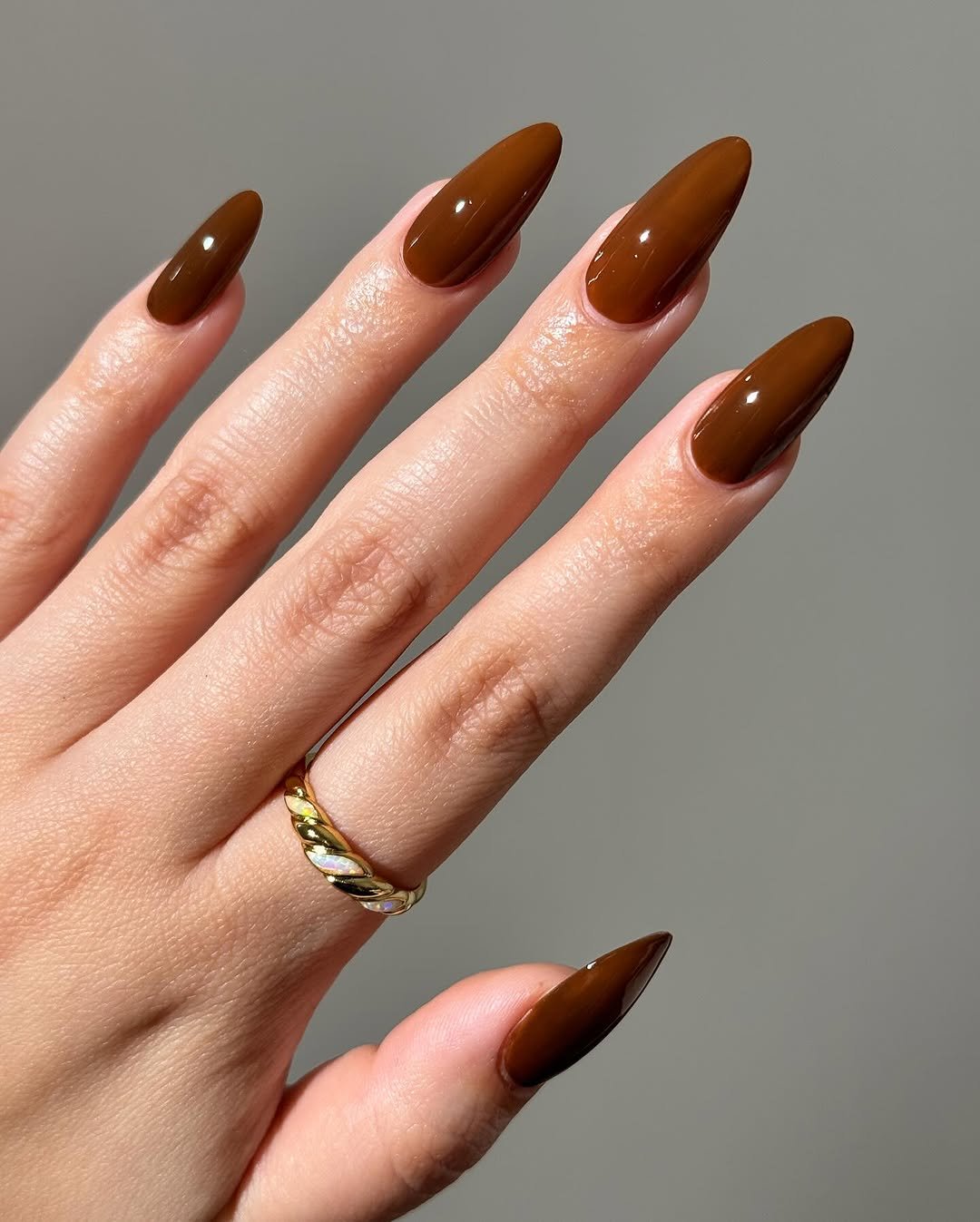 unhas básicas esmaltadas em marrom escuro, anel dourado no dedo anelar.