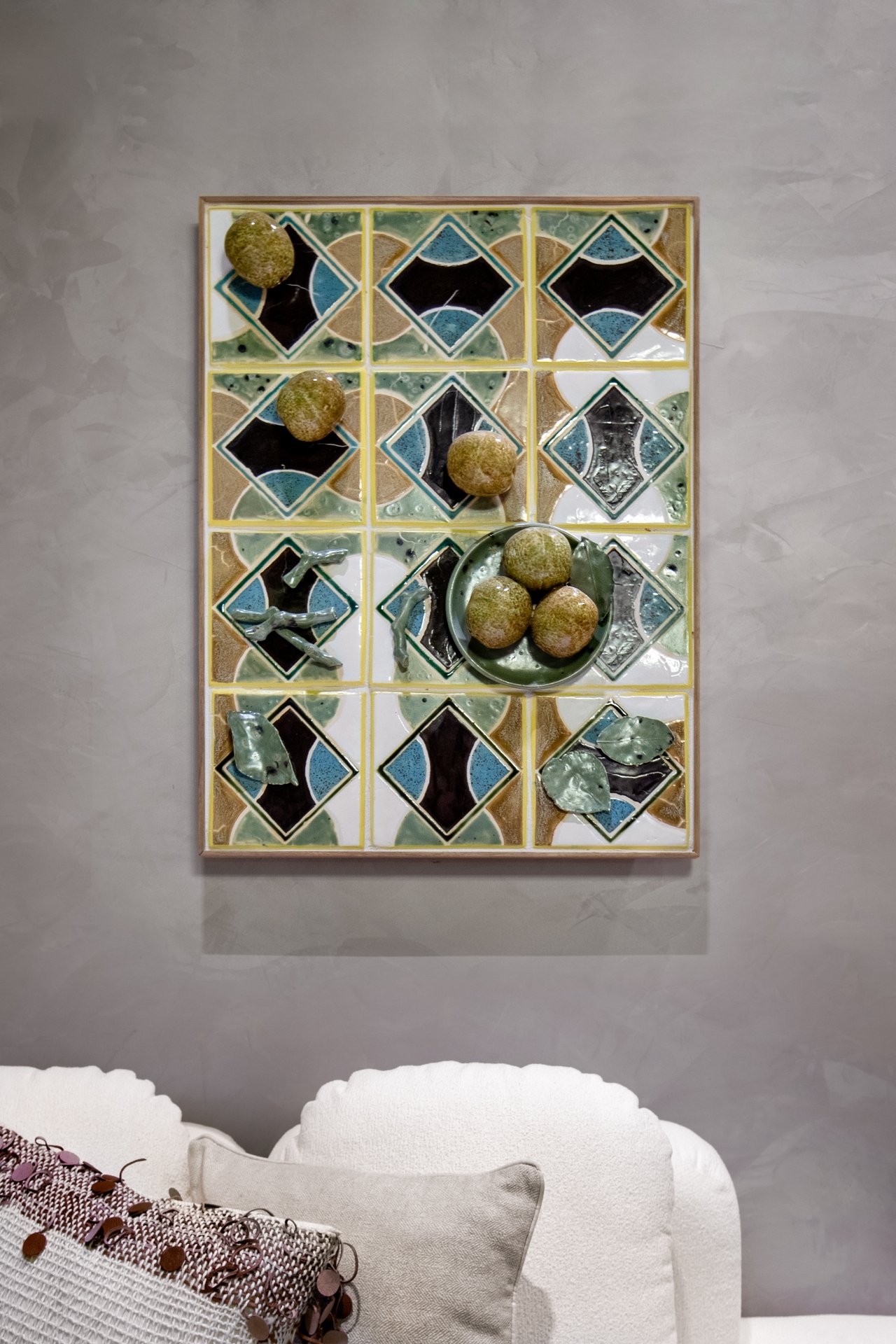 Painel de azulejos geométricos com detalhes verdes, decorado com esferas em relevo, acima de um sofá claro. Verde na decoração