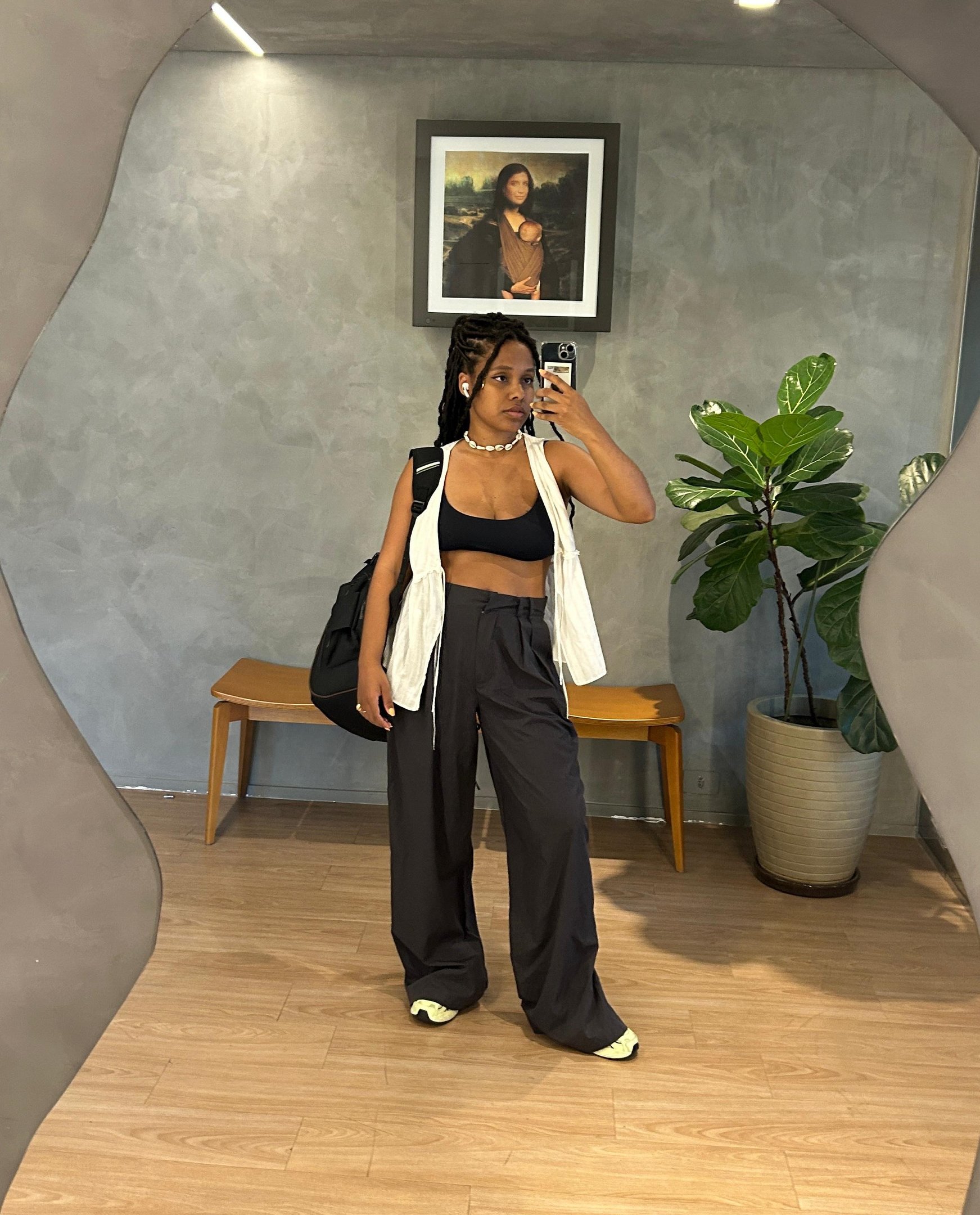Mulher em frente a espelho vestindo calça larga e top. Look moderno e confortável ao lado de planta.