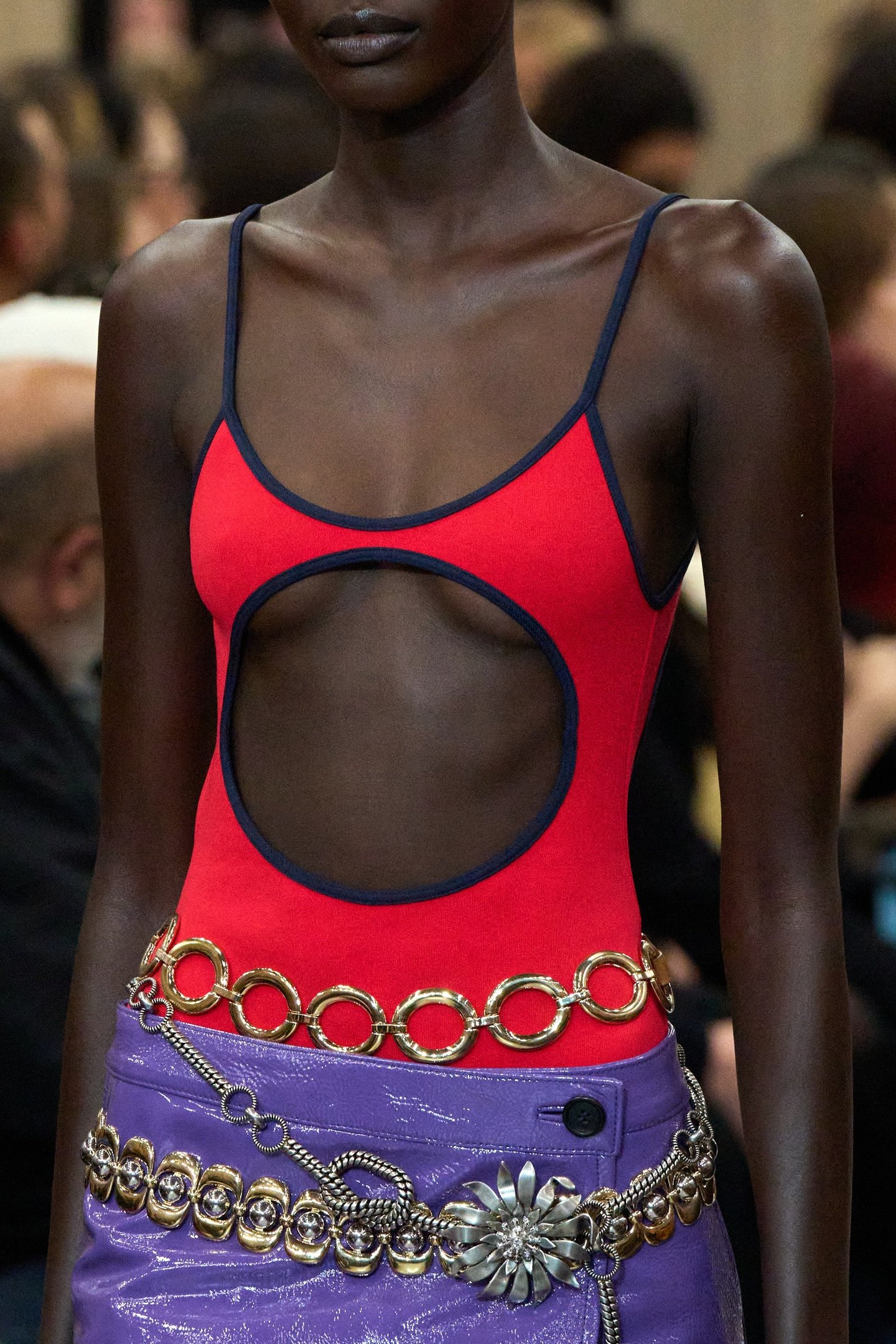 Modelo veste top vermelho com recorte, saia roxa e cintos de correntes, tendência de moda de 2025.
