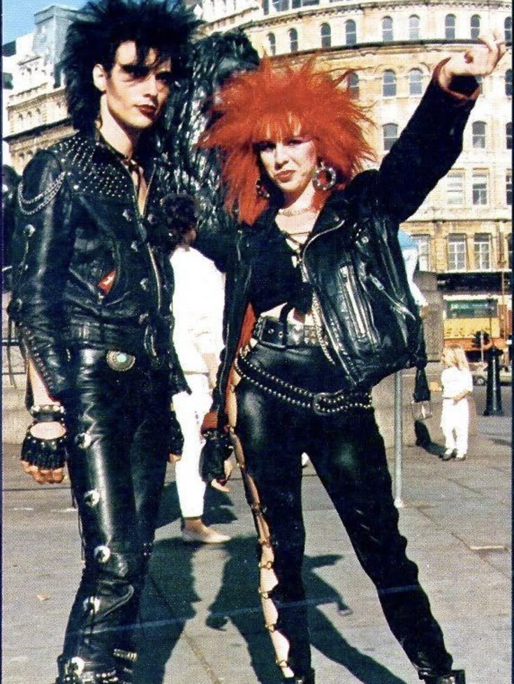 Pessoas em roupas de couro preto e penteados punk vibrantes, lembrando estilo ousado dos anos 1980.