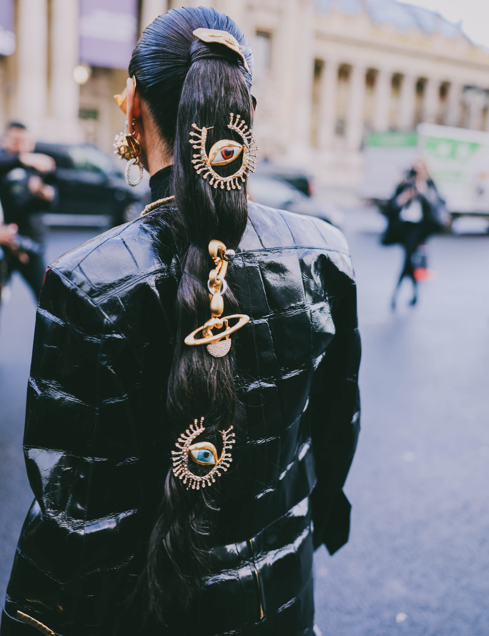 penteado com acessórios maximalistas no cabelo, incluindo enfeites dourados em forma de olho e planetas.
