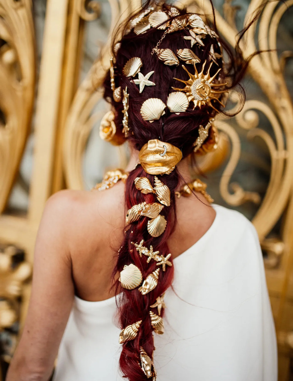 Cabelo adornado com acessórios maximalistas dourados em forma de conchas e estrelas-do-mar.