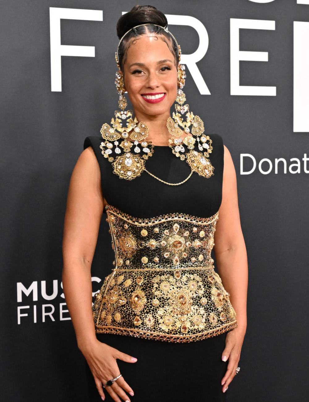 Mulher usando acessórios maximalistas no cabelo e corselete dourado ornamentado. Ela veste um vestido preto elegante.