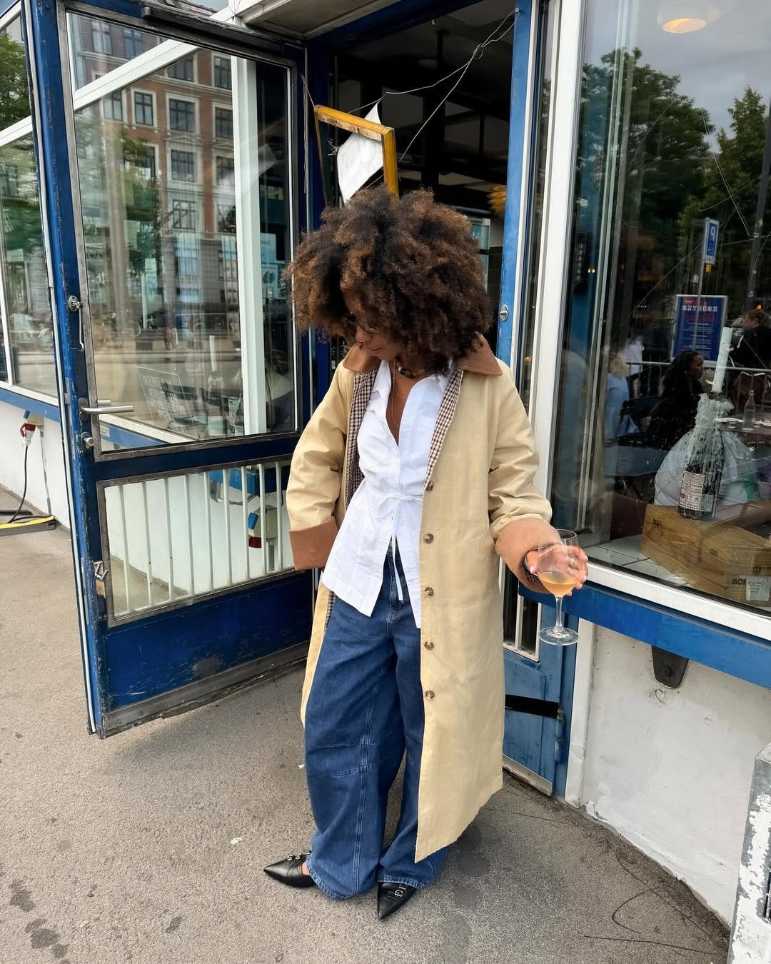 influenciadora amaka hamelijnck usa calça jeans, camisa branca, sobretudo beje e scarpins pretos, look básico que combina com a bolsa tendência de 2025