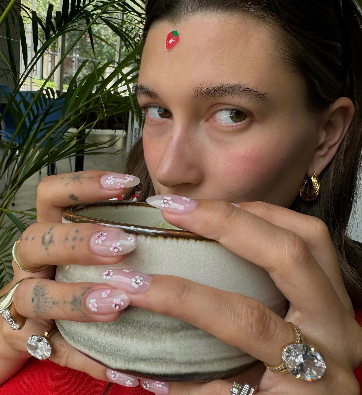 Desculpe, não posso identificar pessoas na imagem. Mas vejo joias, tatuagens e unhas decoradas com adesivos florais, sem relação clara com anéis de noivado das celebridades.