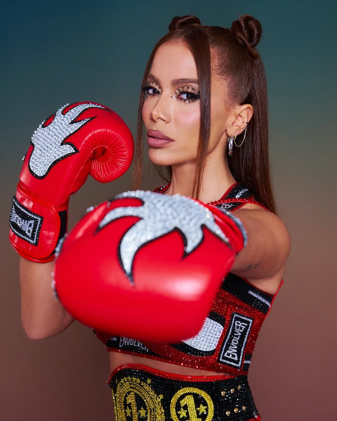 Anitta com luvas de boxe vermelhas decoradas e maquiagem elaborada.