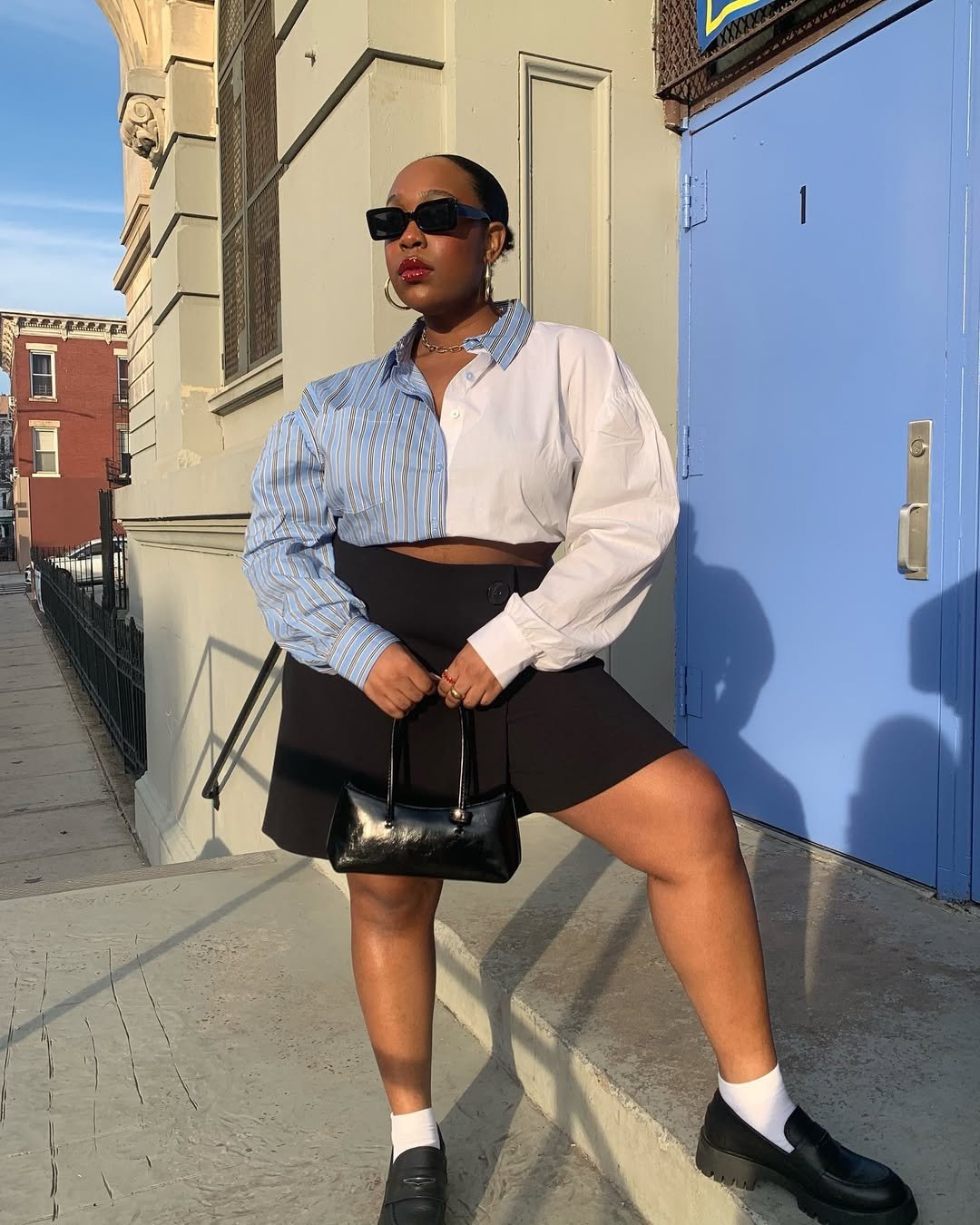Influenciadora Aniyah Morinia usa look saia preta, camisa listrada e mocassim com meia, tendências de sapatos para o inverno
