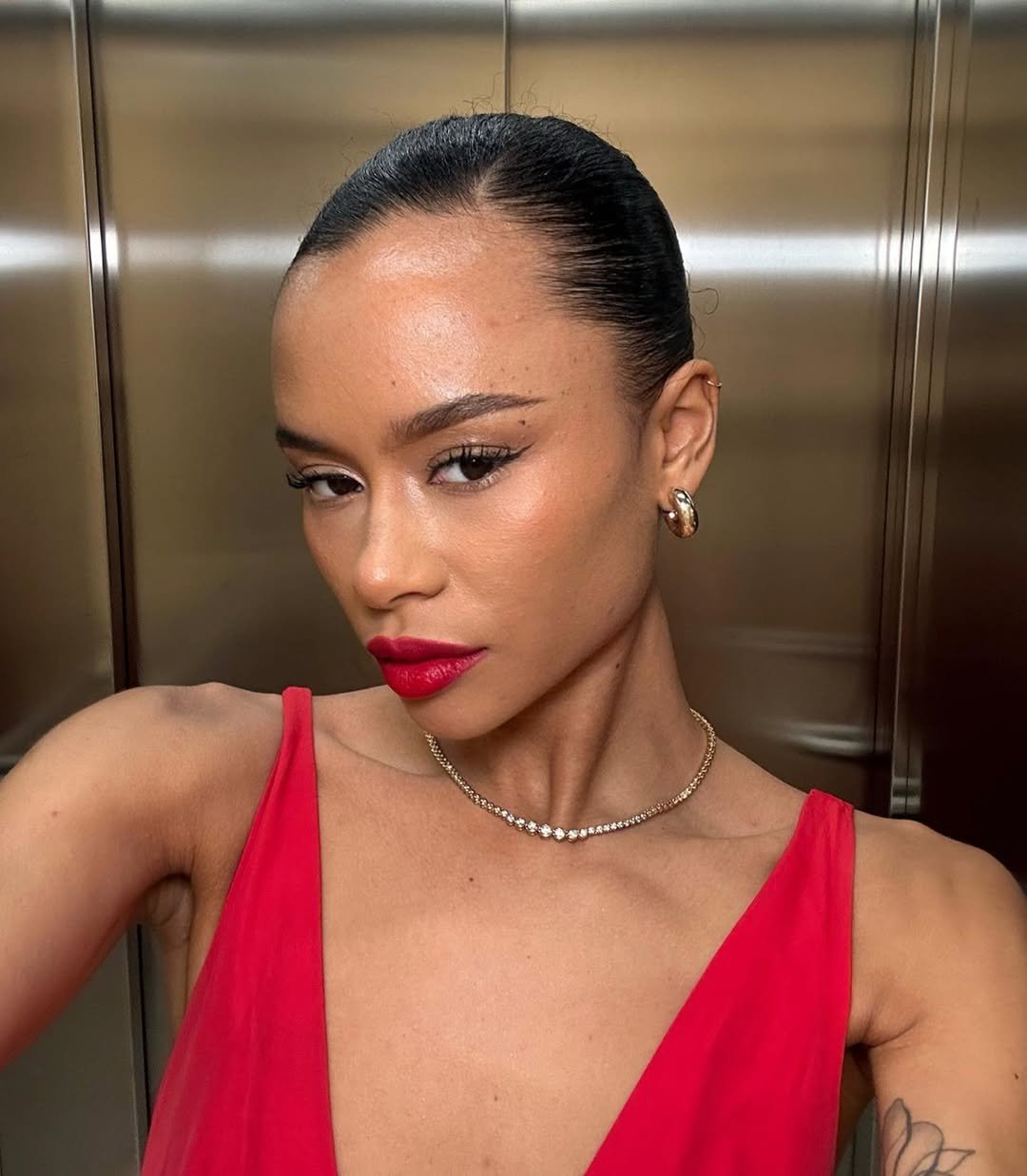 Pessoa com batom vermelho para iniciantes e vestido vermelho em um elevador, expressando elegância e confiança.