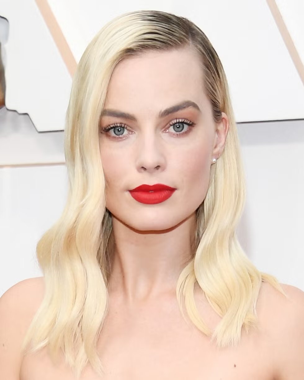 Pessoa com cabelo loiro ondulado e batom vermelho vibrante, destacando um look clássico e elegante.