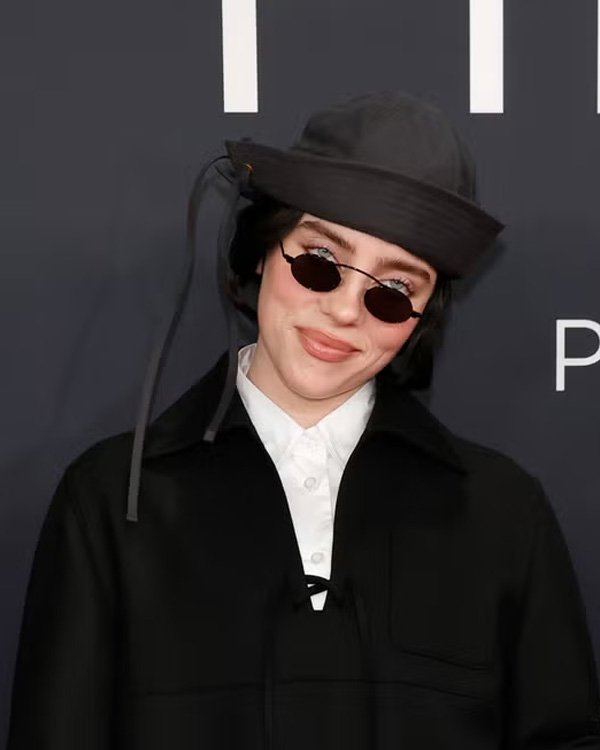 Pessoa usando óculos de sol pequenos, chapéu estiloso e jaqueta preta. Acessório tendência 2025 com visual moderno.
