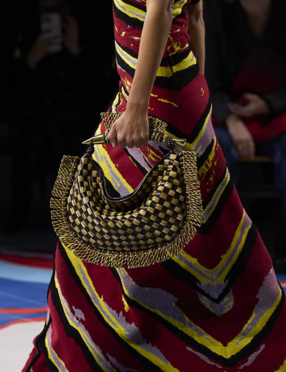 Bolsa xadrez com detalhes trançados dourados, combinando com vestido colorido, exemplifica bolsas tendência 2025.
