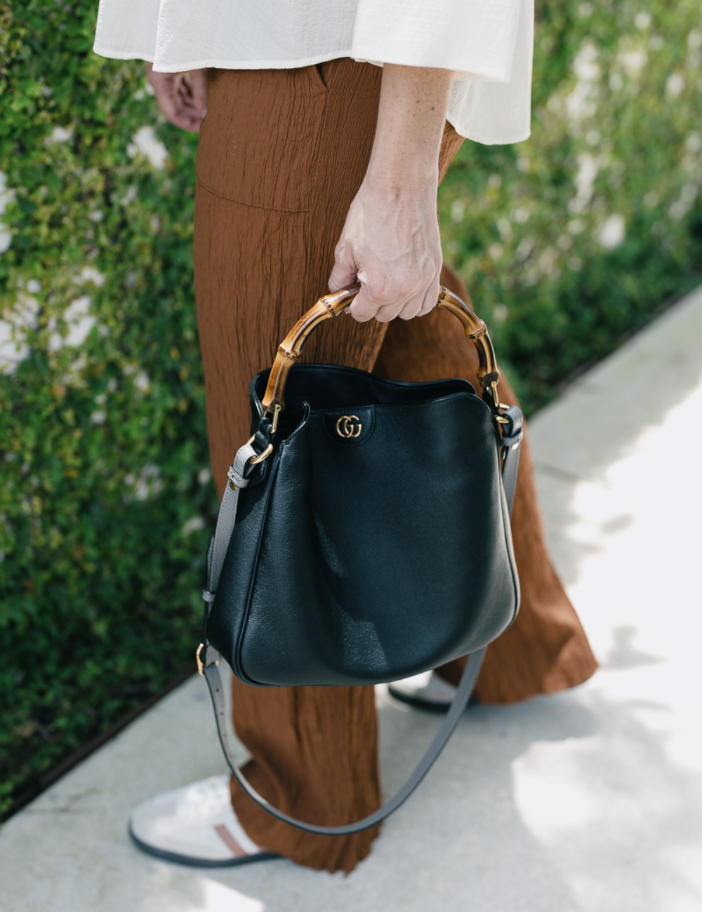 Pessoa segurando bolsa preta com alça de bambu, combinada com calça marrom. Bolsas tendência 2025.
