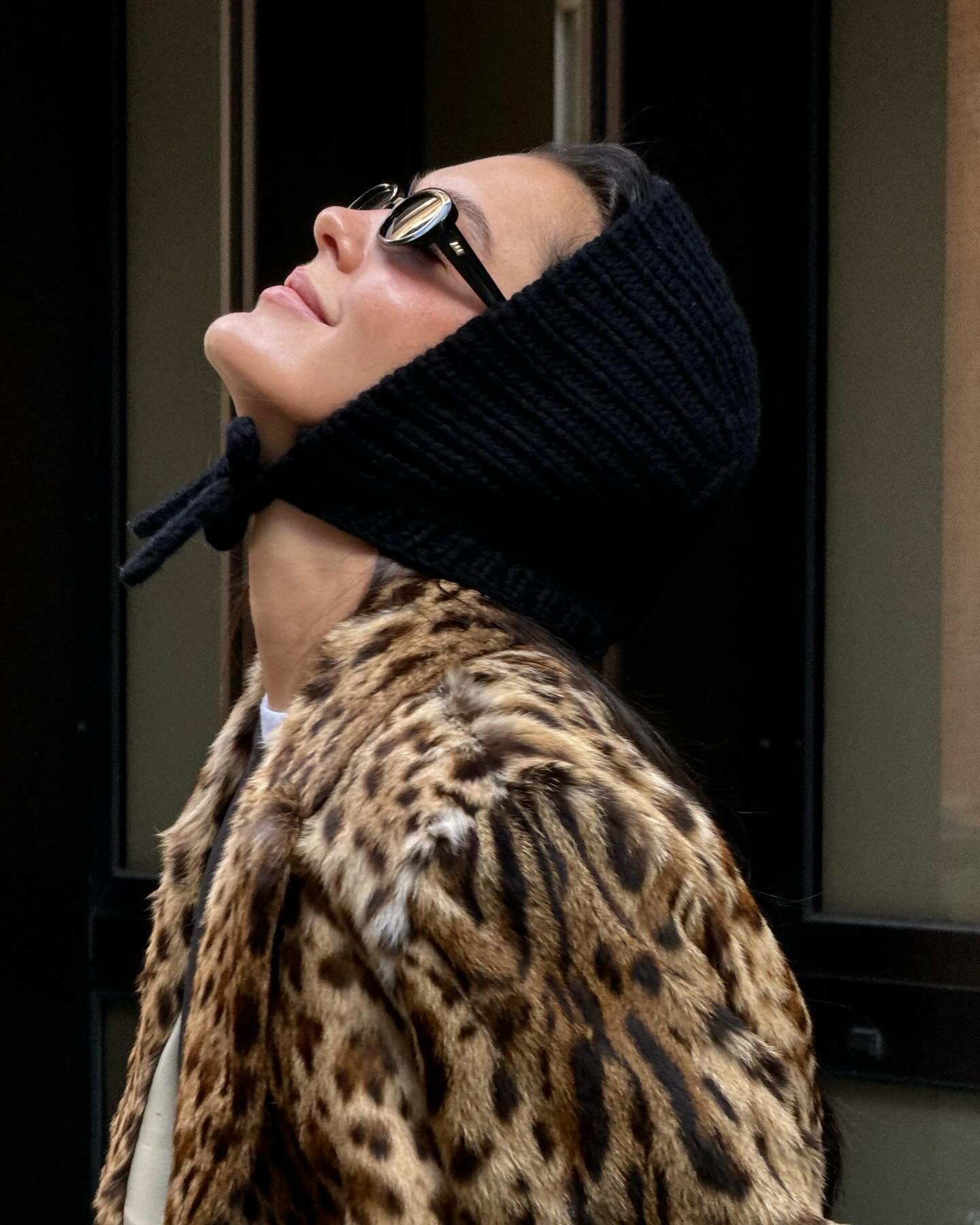 Mulher usando óculos escuros e uma touca preta de tricô, em casaco de estampa de leopardo.