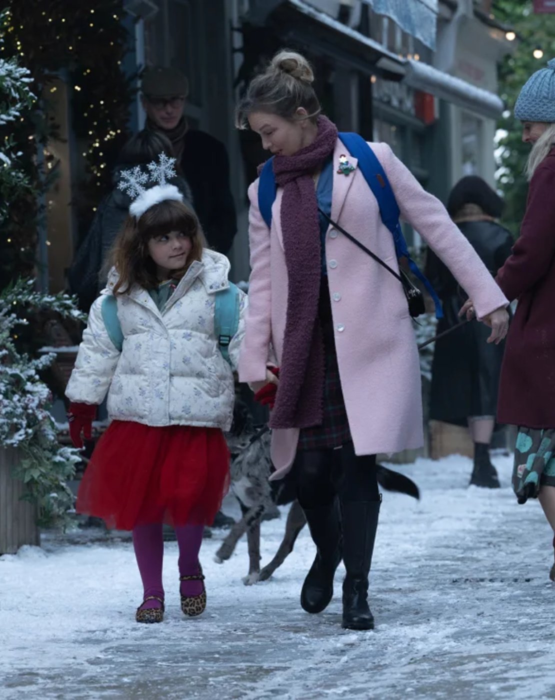 Bridget Jones e uma criança caminham na neve com roupas de inverno.