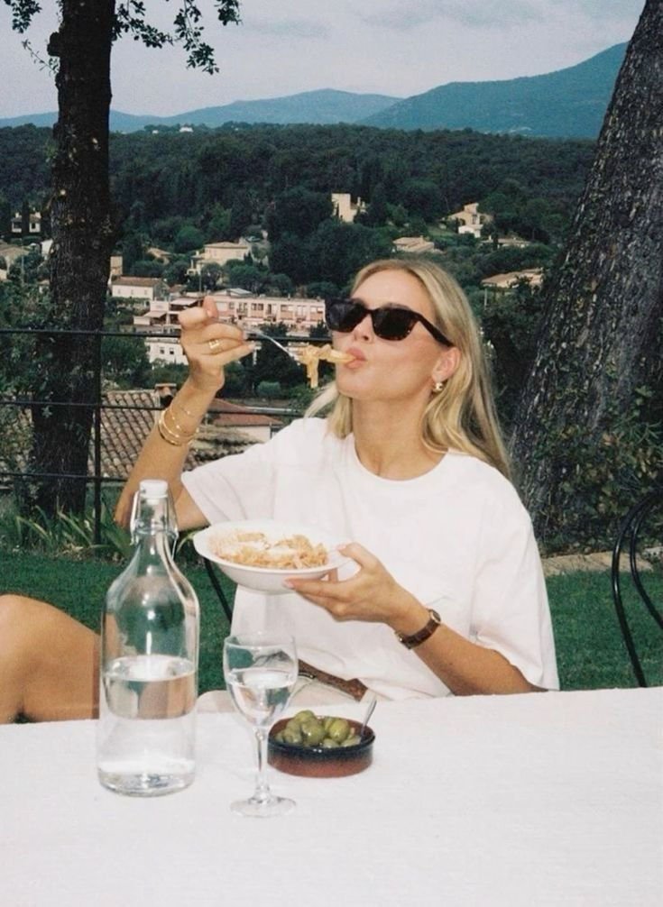 Pessoa comendo ao ar livre, cercada por paisagem natural cênica. Elemento de pausa em meio a ciclos.