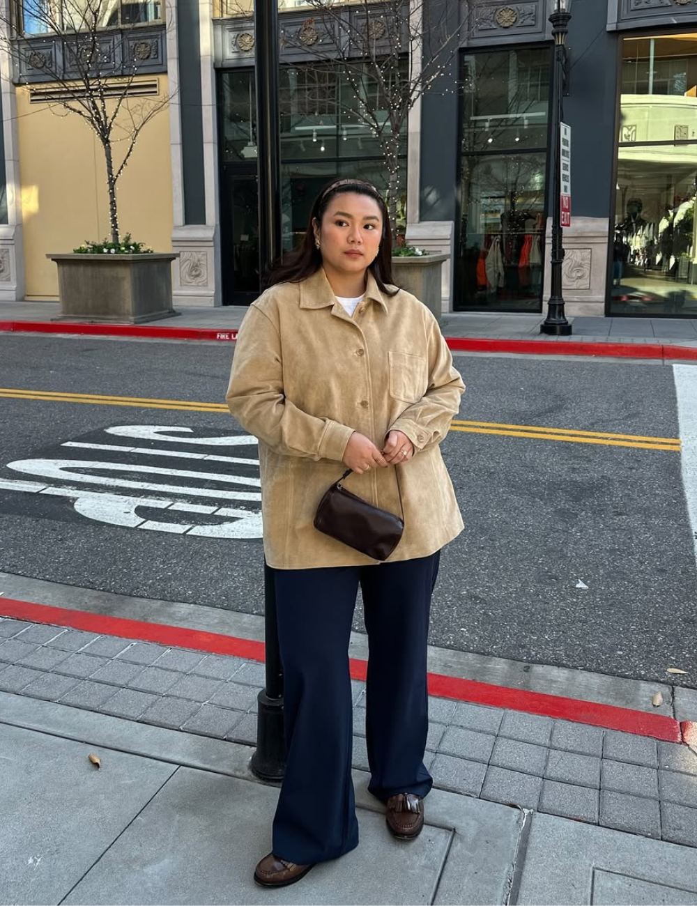 Pessoa com casaco bege e calça escura segura bolsa marrom. Sapato marrom elegante complementa o look casual na rua.