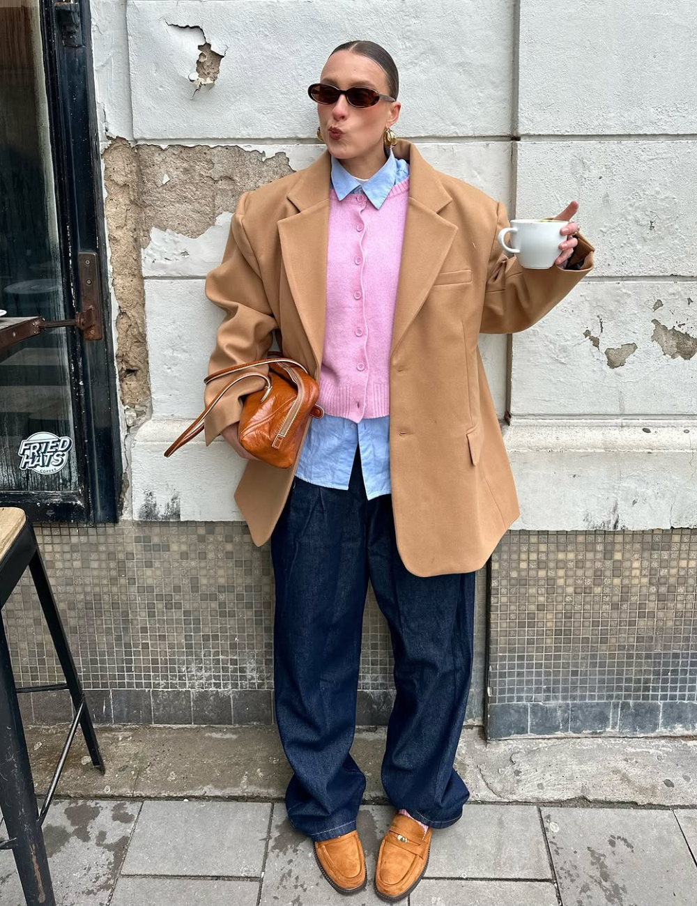 Pessoa em traje casual chique, segurando bolsa e café. Calça jeans, casaco bege e sapato elegante marrom.