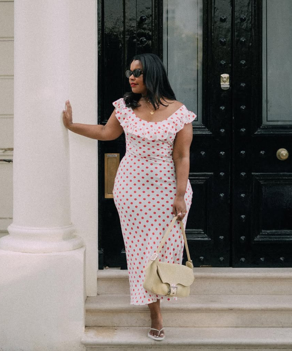 Vestido branco com estampa poá vermelha sendo usado por uma pessoa, em frente a uma porta preta.