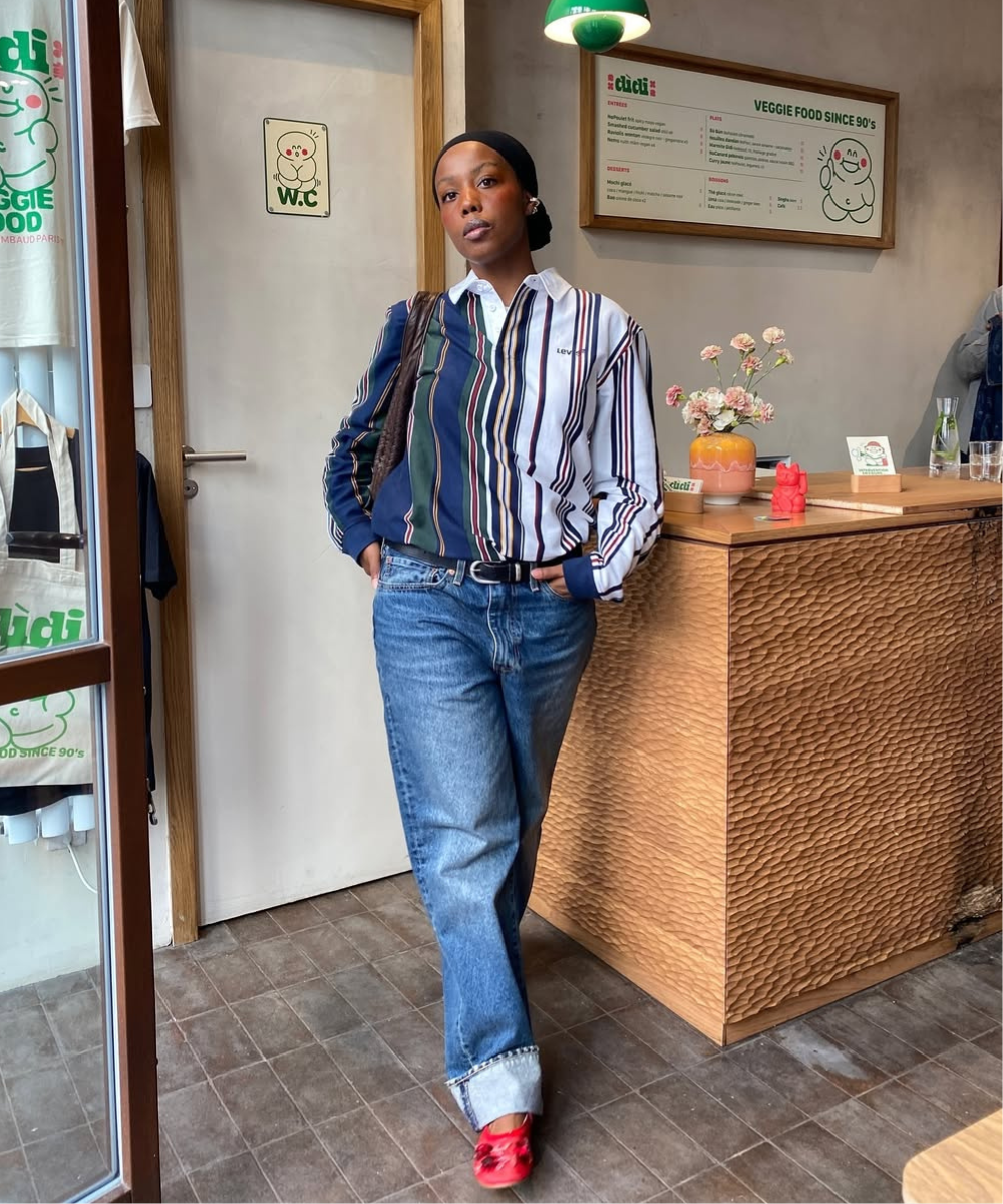 Pessoa usando camisa listrada e jeans em loja de comida vegetariana, com sapatilhas vermelhas modernas.