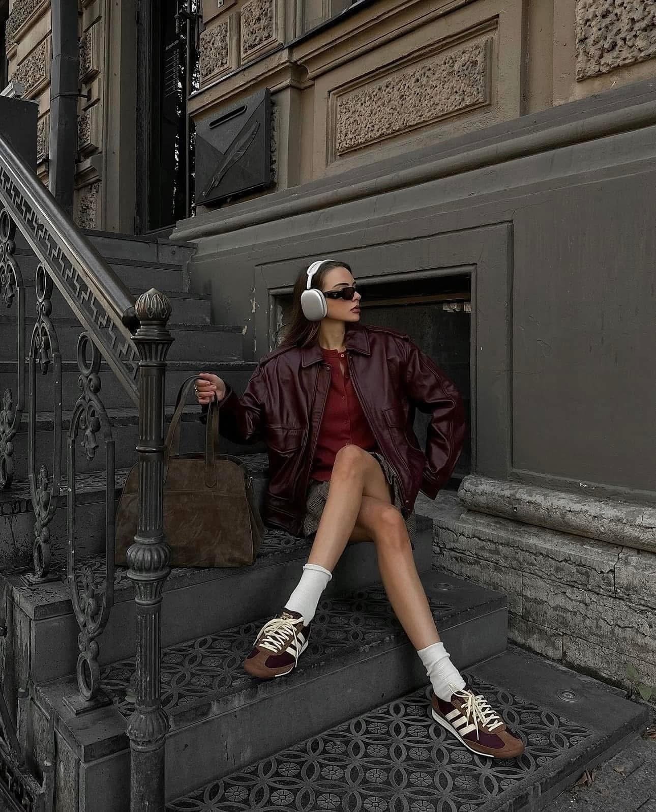 Pessoa sentada em escada usando jaqueta marrom, tênis marrom e fones de ouvido grandes.