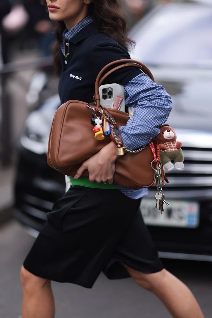 Mulher carregando bolsa de couro marrom, estilo doctor bags, com chaveiros e celular.