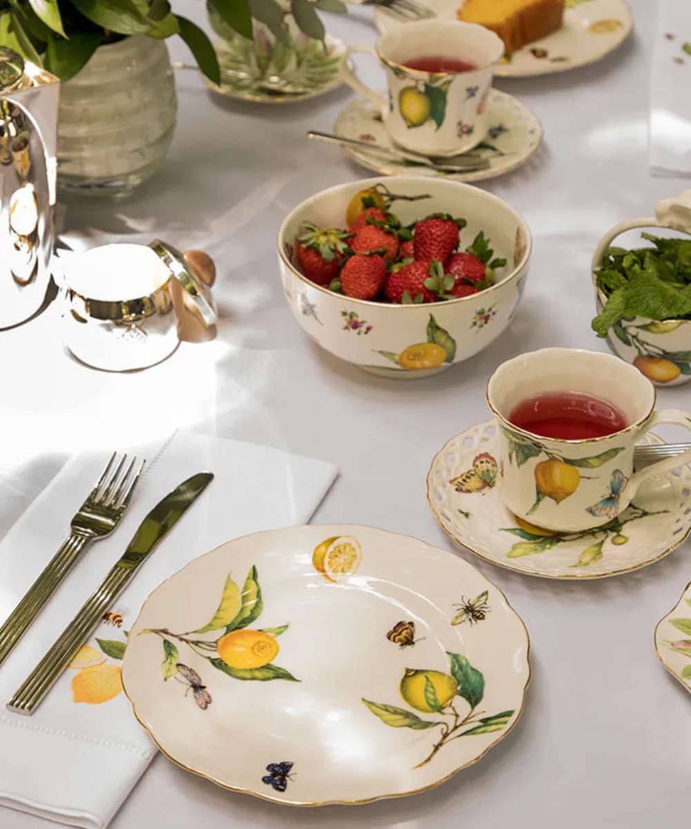 Louça decorada com frutas cítricas e borboletas em uma mesa posta para chá com morangos. Mostra duppies na moda.