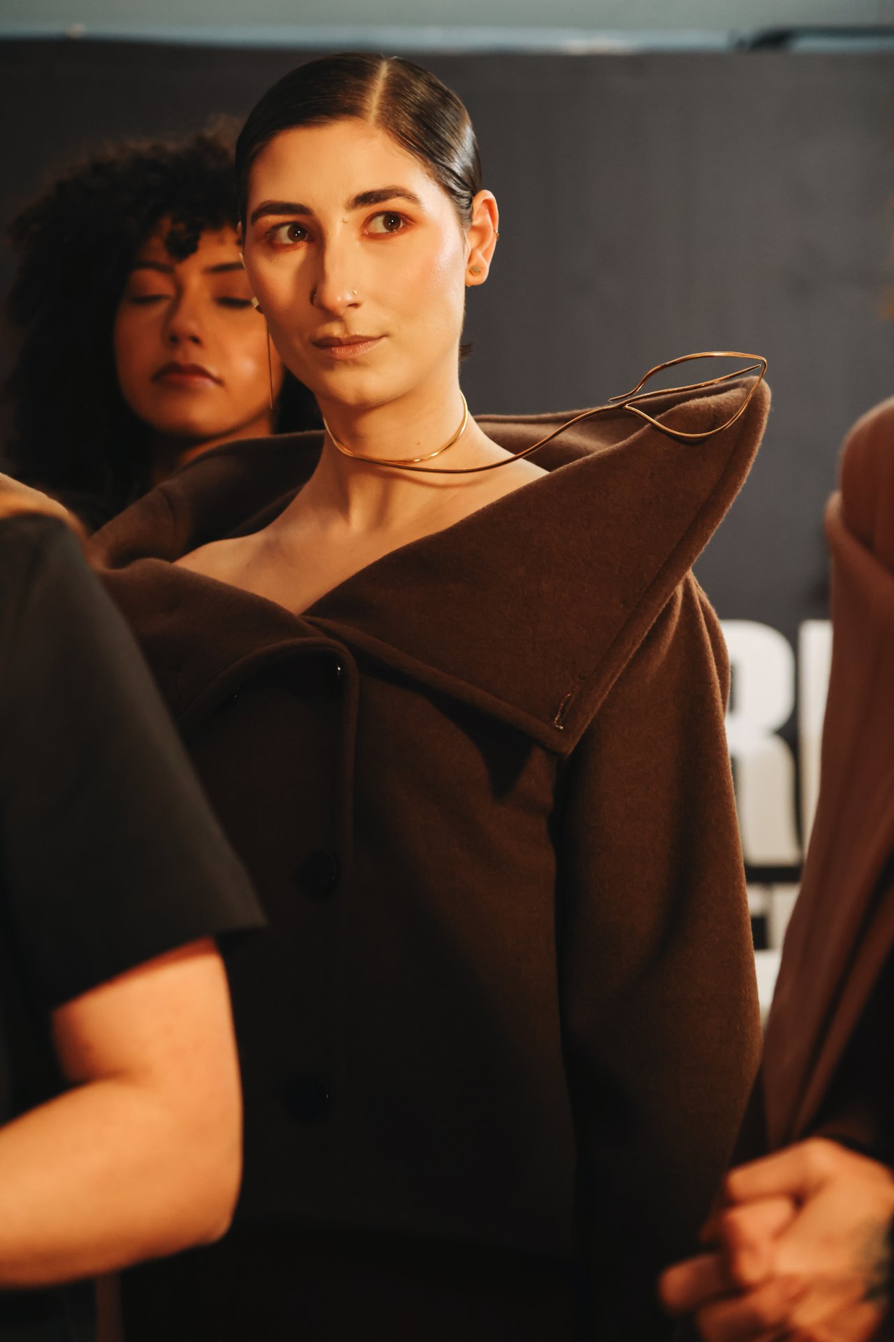 Modelo usando casaco marrom com colar metálico sofisticado, característico do estilo Eleonora Hsiung.