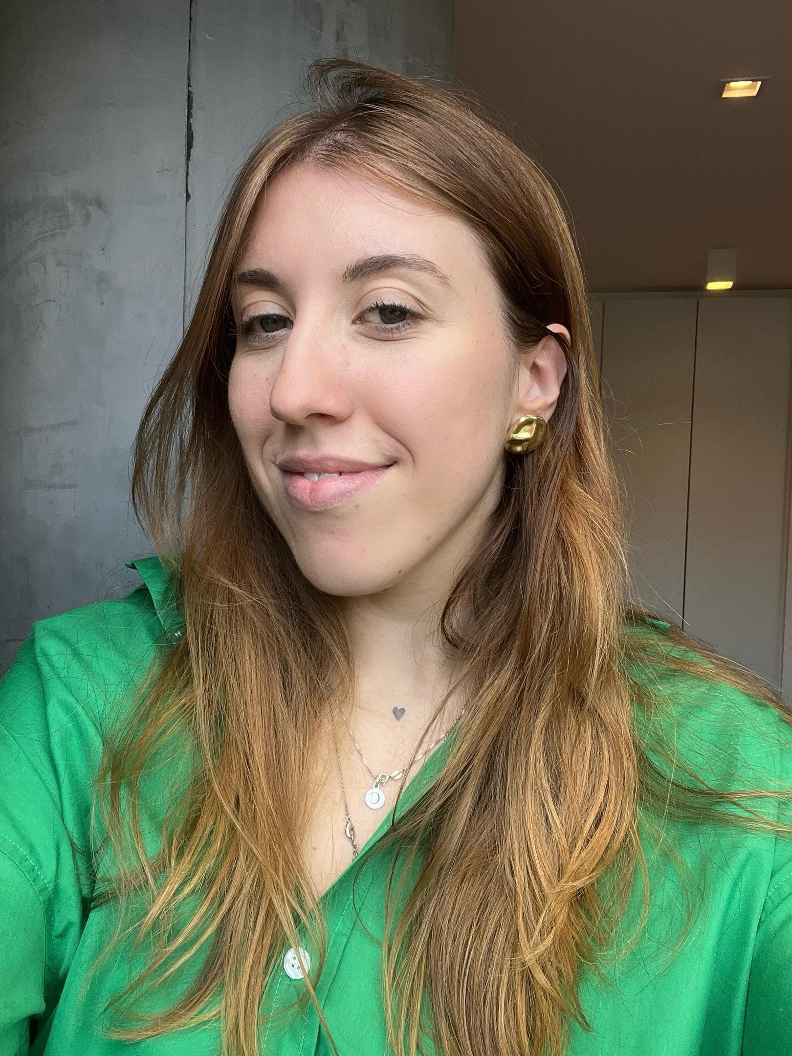 A mulher sorridente usa camisa verde em ambiente interno, transmitindo bem-estar e cílios crescerem naturalmente.