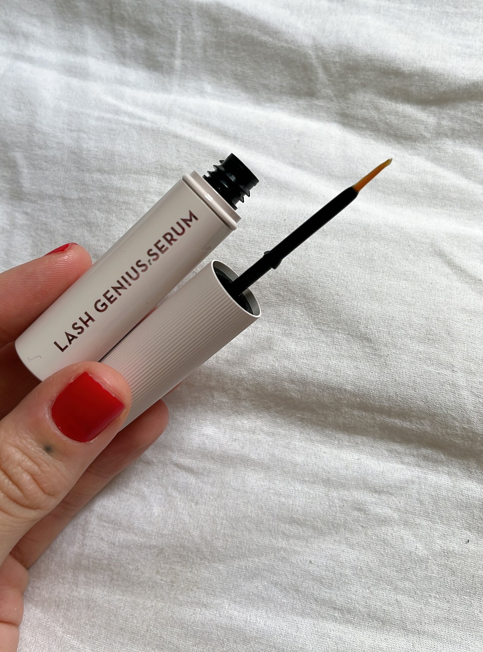 Sérum para impulsionar o crescimento dos cílios segurado por uma mão com unhas pintadas de vermelho.