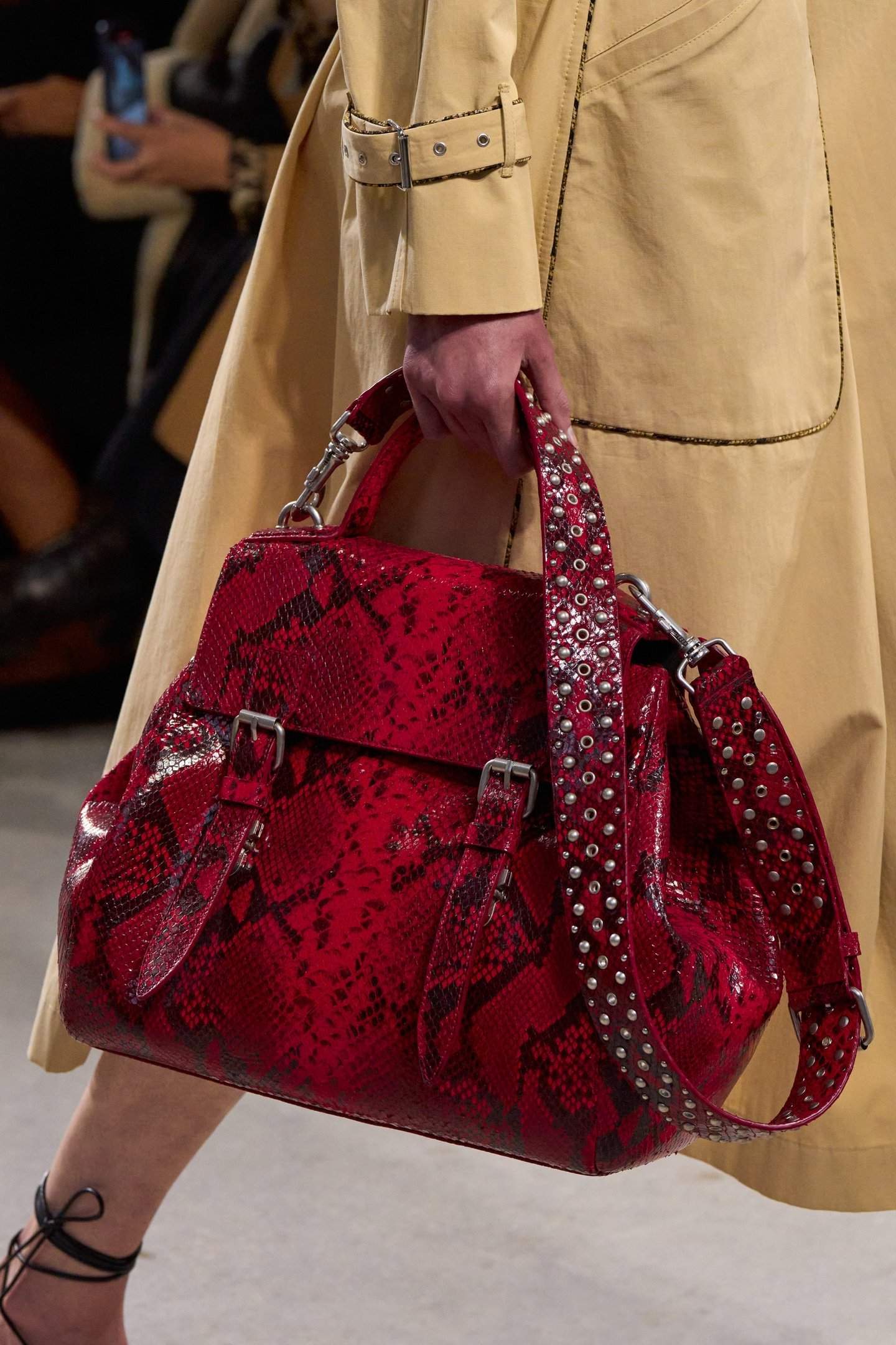 Bolsa vermelha com estampa de cobra e detalhes de tachas, combinada com um casaco bege.